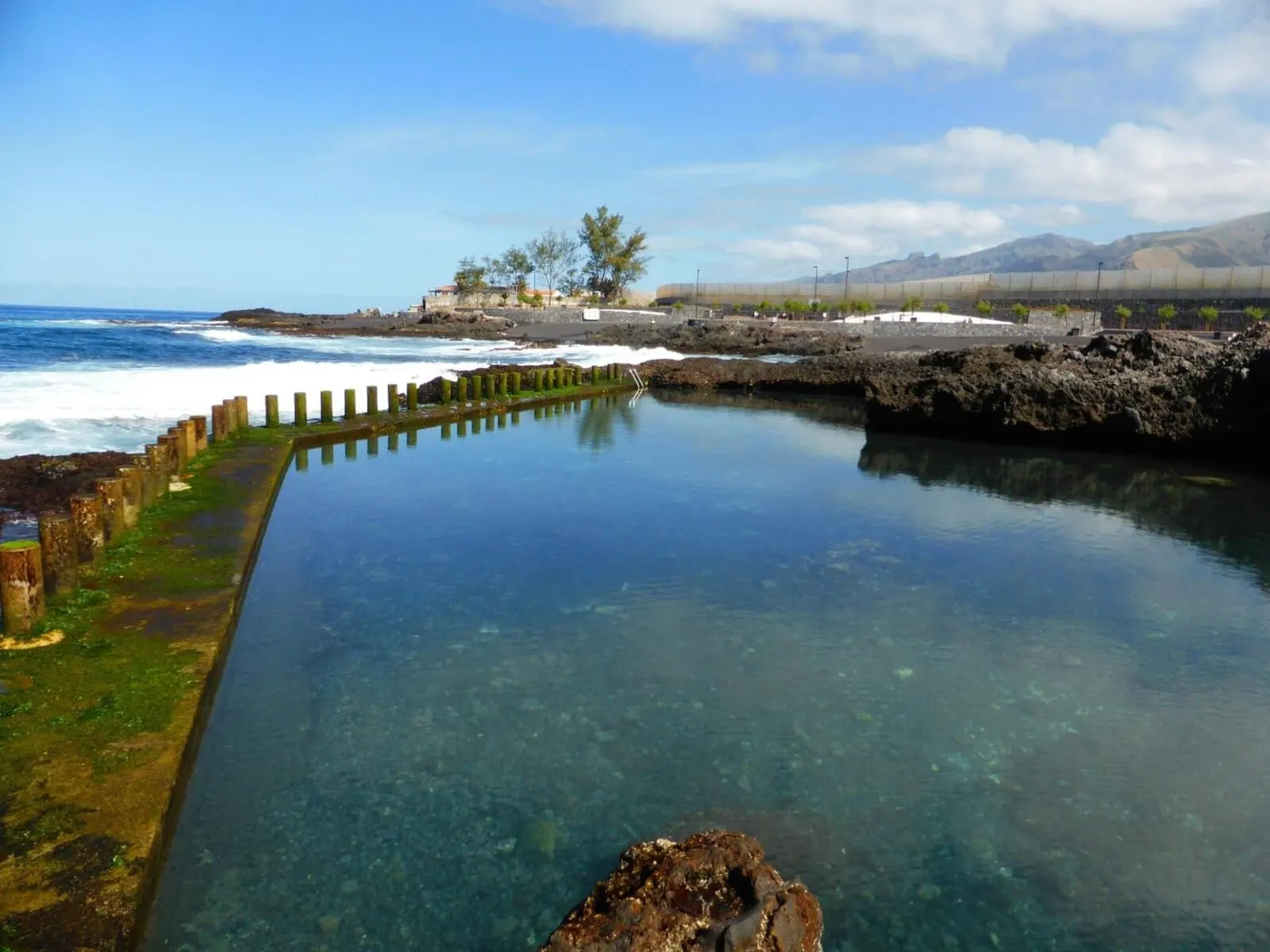Hotel Rural El Navío: A clear pool with a rocky edge, a view of the ocean, and a distant mountain range