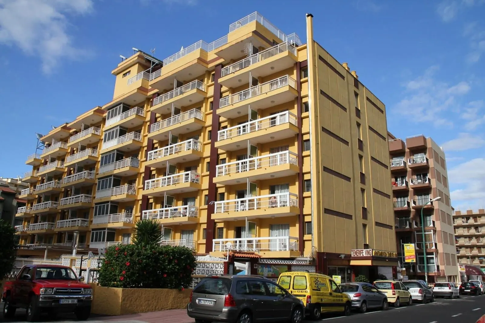 Skyview Hotel by LIVVO: A multi-story yellow building with balconies, a red car parked in front