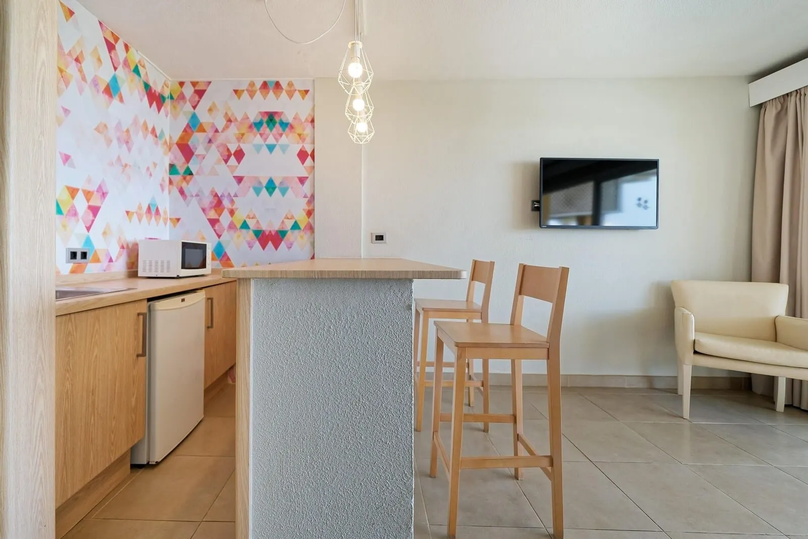 Servatur Isora Suites: A modern kitchen with a built-in island, wooden chairs, a sofa