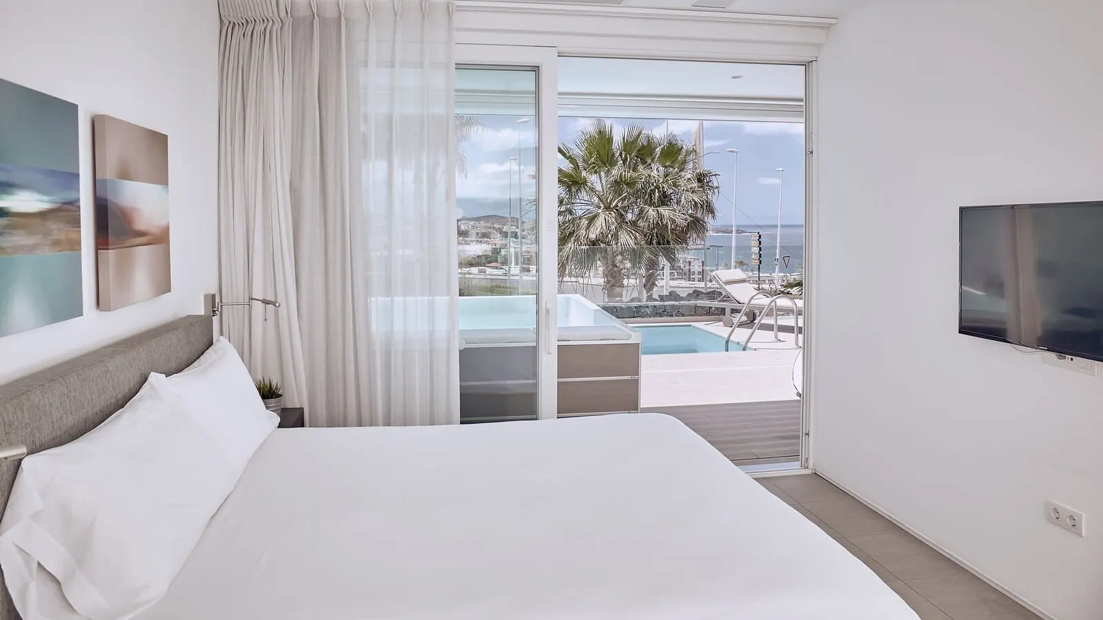 Domes Baobab Suites: A hotel room with a bed, a TV, a balcony with a pool, and a view of the city