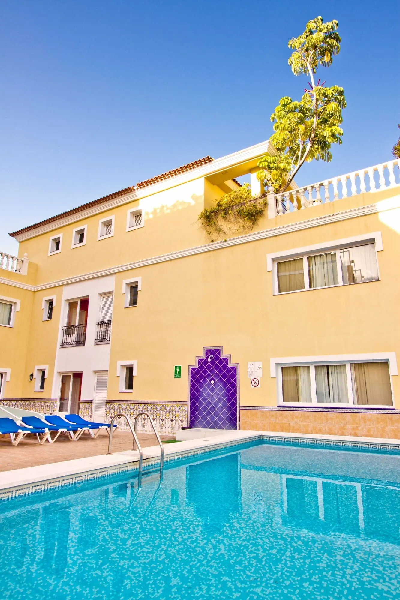 RF Apartamentos Bambi: A hotel with a swimming pool, a purple gate, and a tree growing on the balcony