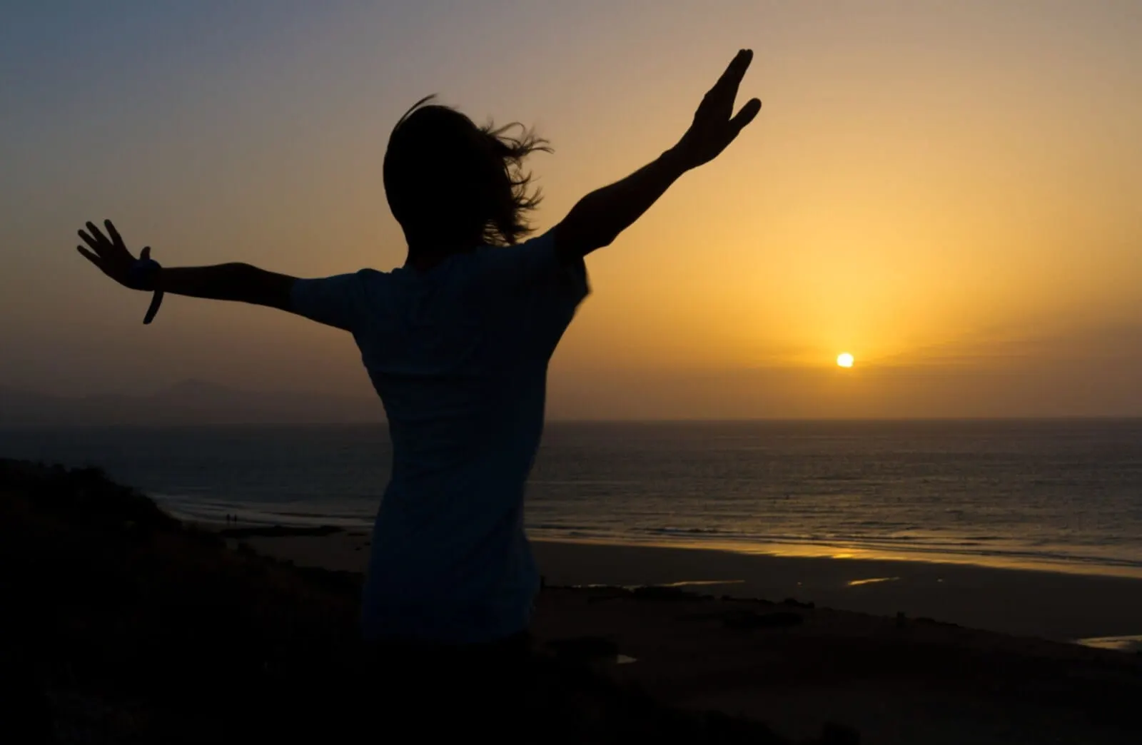 HOVIMA Suites Costa Adeje: A silhouette of a person with arms raised against a sunset at the beach