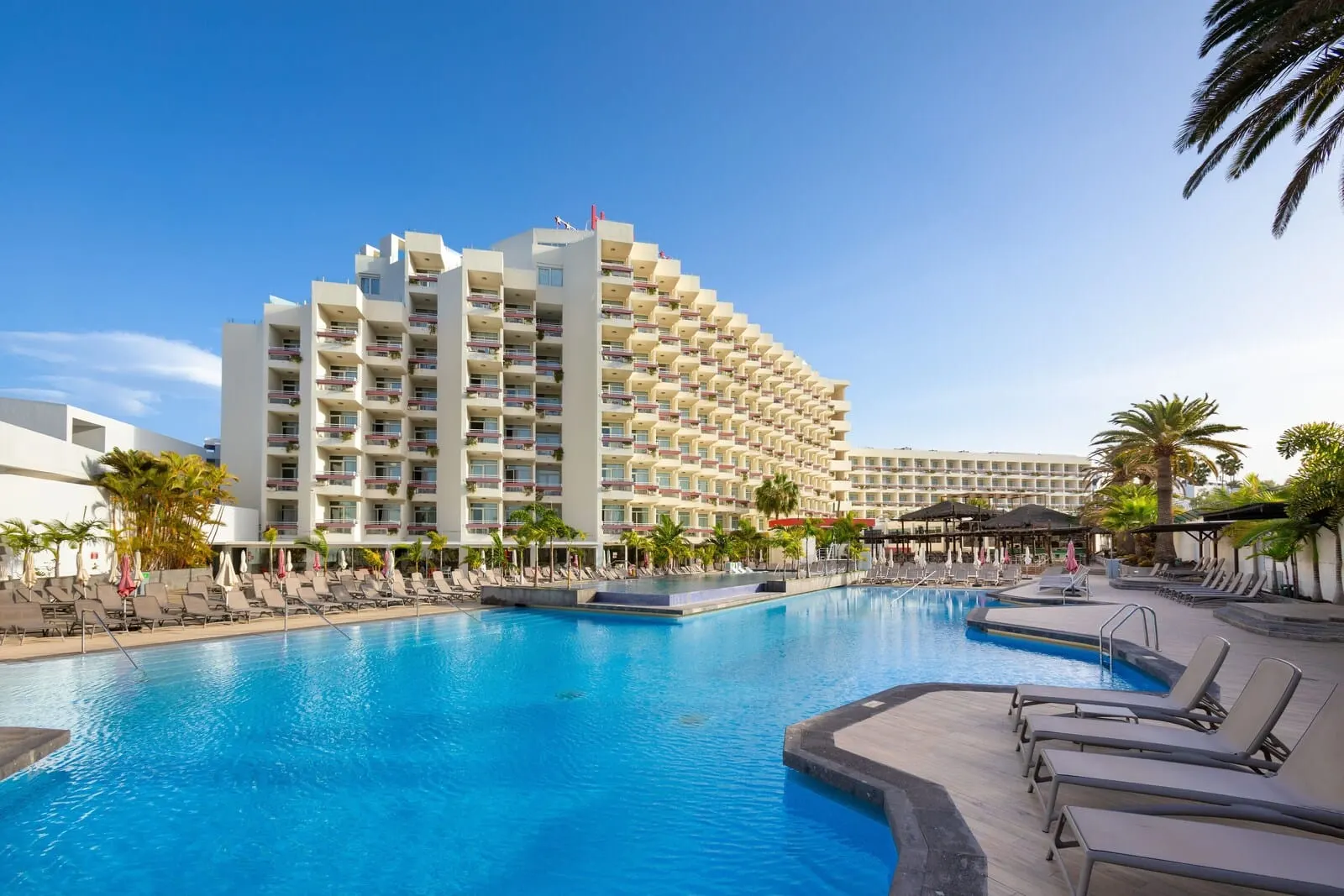 Alexandre Troya: A hotel with a large pool area, multiple balconies, and a clear blue sky