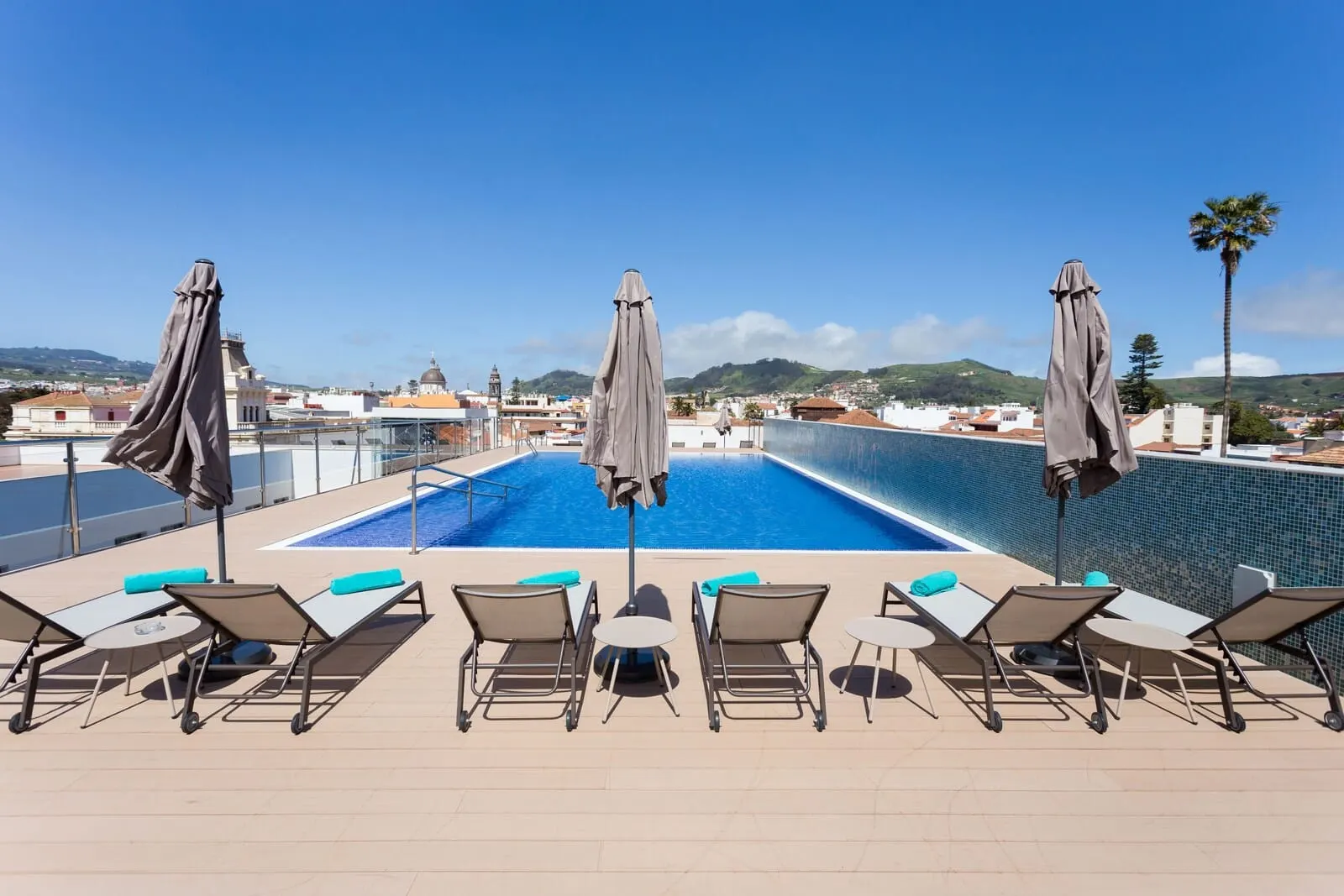La Laguna Gran Hotel: A rooftop pool area with lounge chairs and umbrellas, overlooking a cityscape and hills