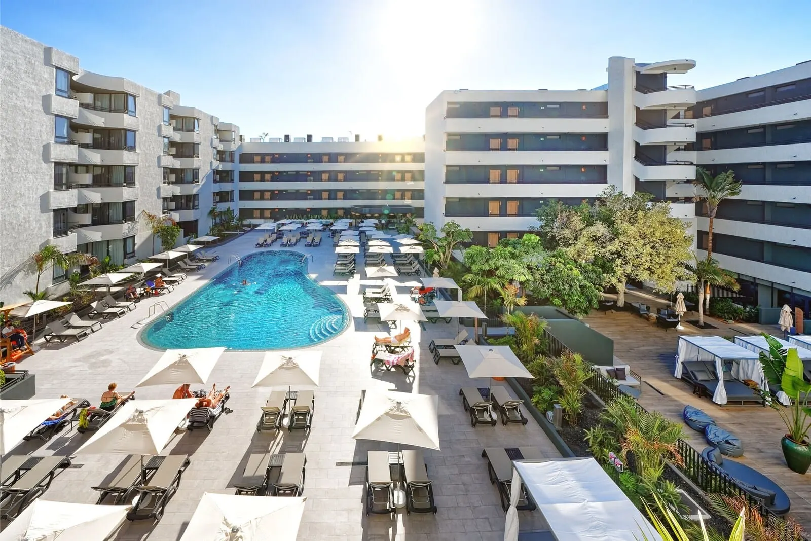 HOVIMA Suites Costa Adeje: A hotel with a central swimming pool surrounded by sun loungers and umbrellas