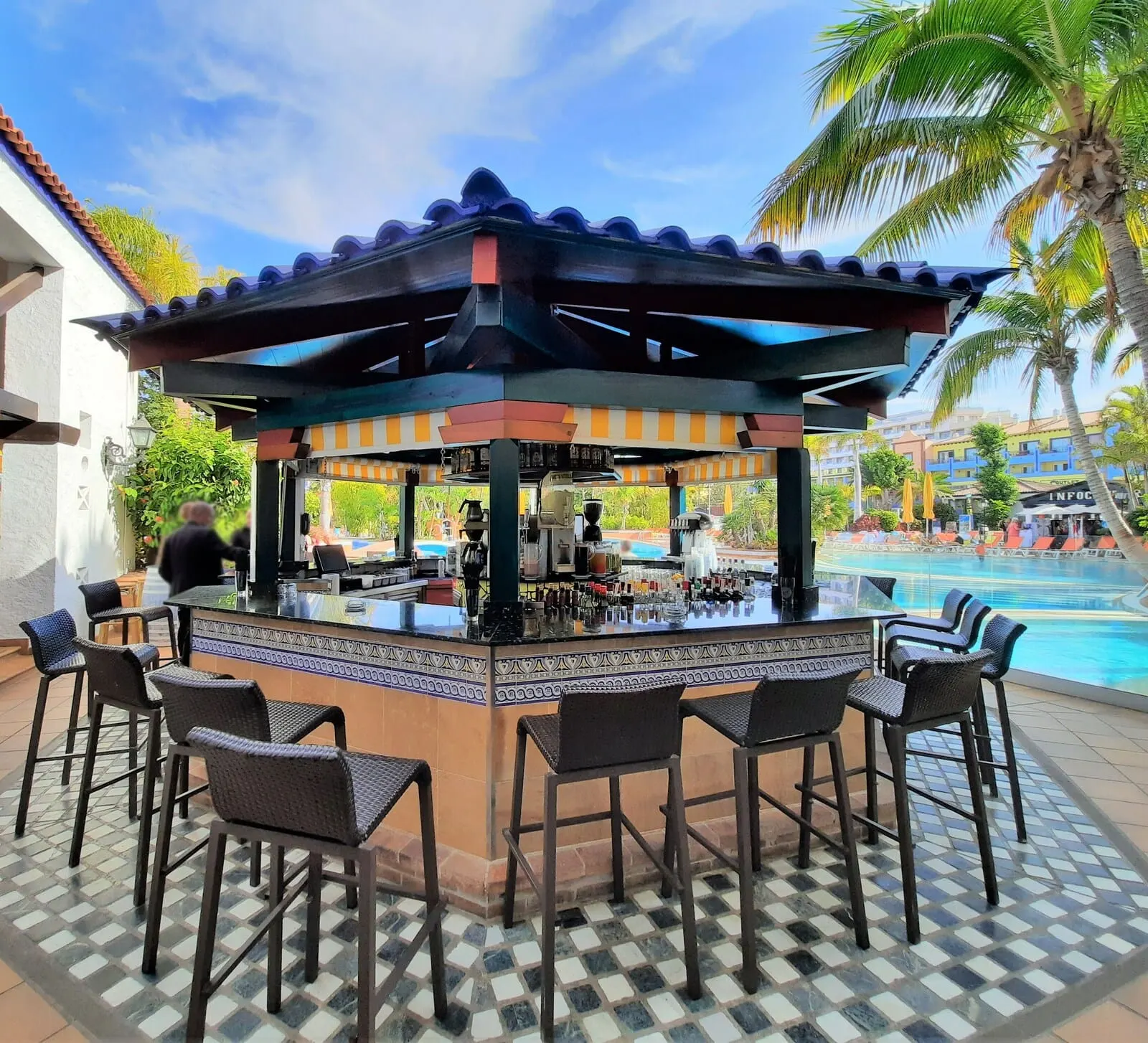 Park Club Europe: An outdoor bar area with a tiled floor, bar stools, and a pool in the background