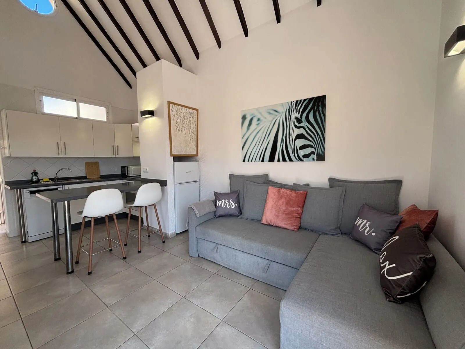 Yucca Park Aparthotel: A modern living room with a grey sofa, a kitchen area with white cabinets