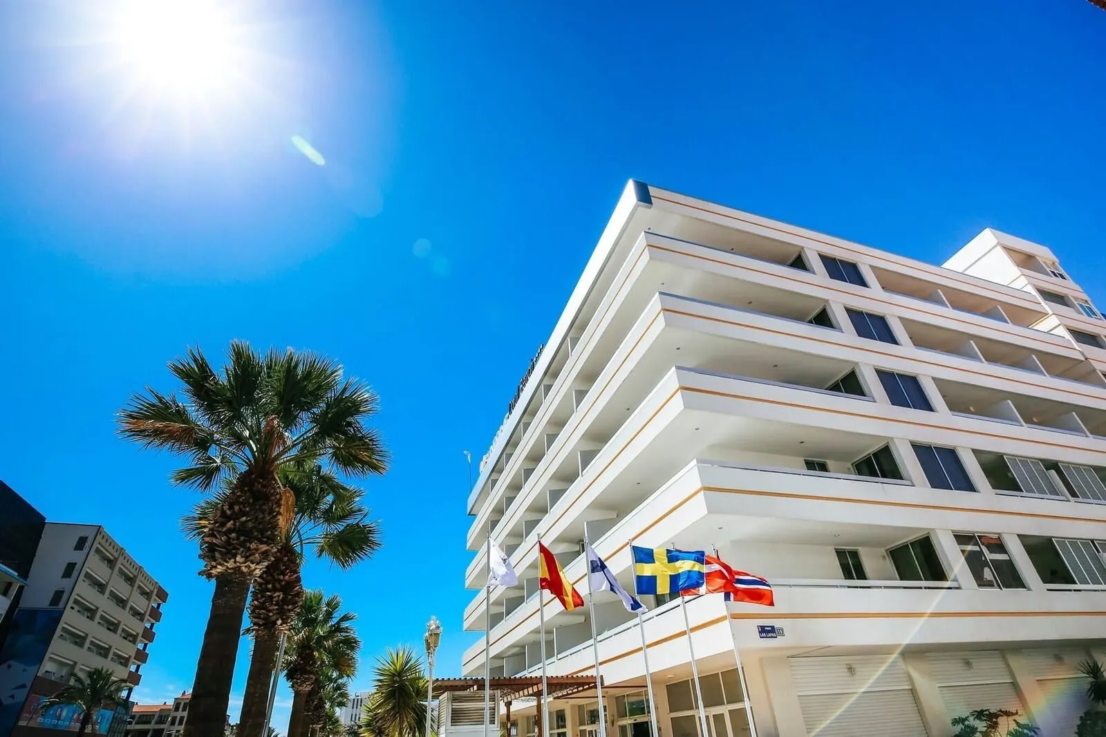 Coral Suites & Spa: A multi-story hotel with balconies, palm trees, and flags