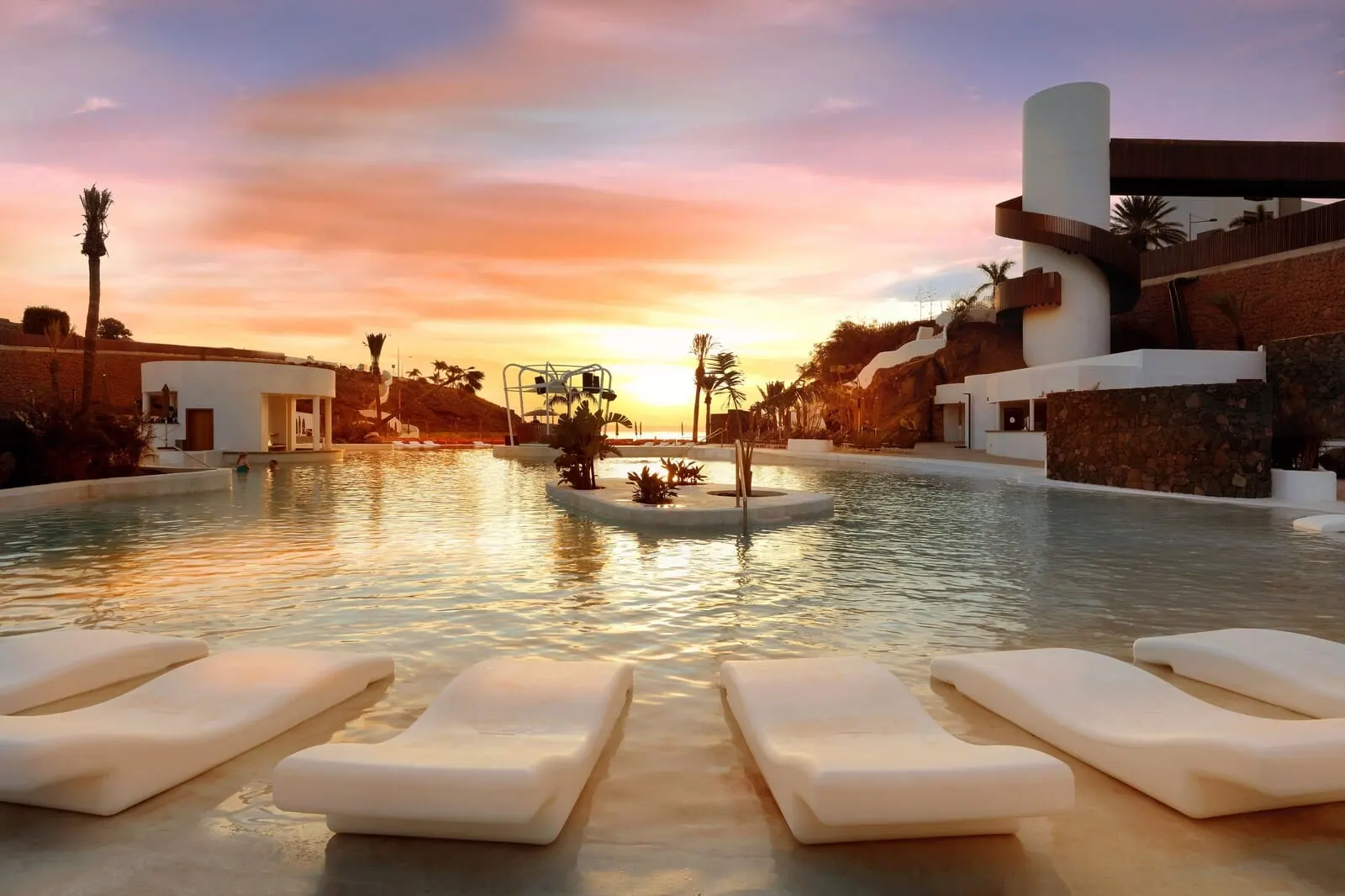 Hard Rock Hotel Tenerife: A pool area with lounge chairs, a water feature, and modern architecture