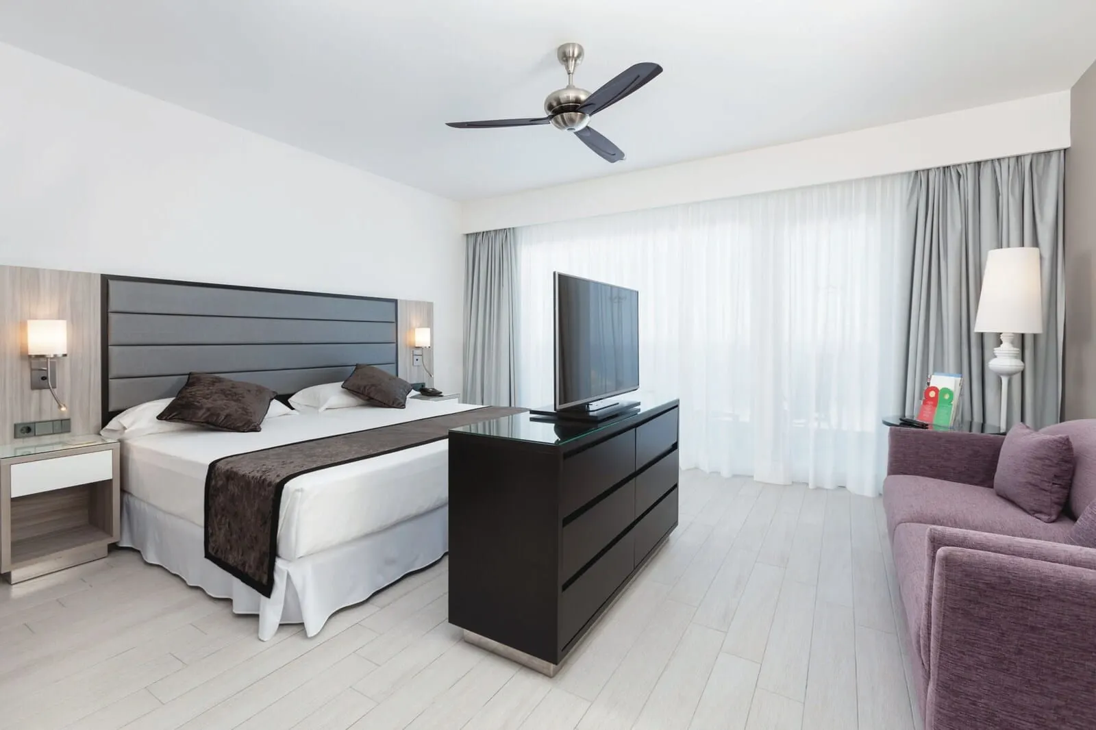 Hotel Riu Palace Tenerife: A modern hotel room with a bed, a TV, a desk, and a sofa