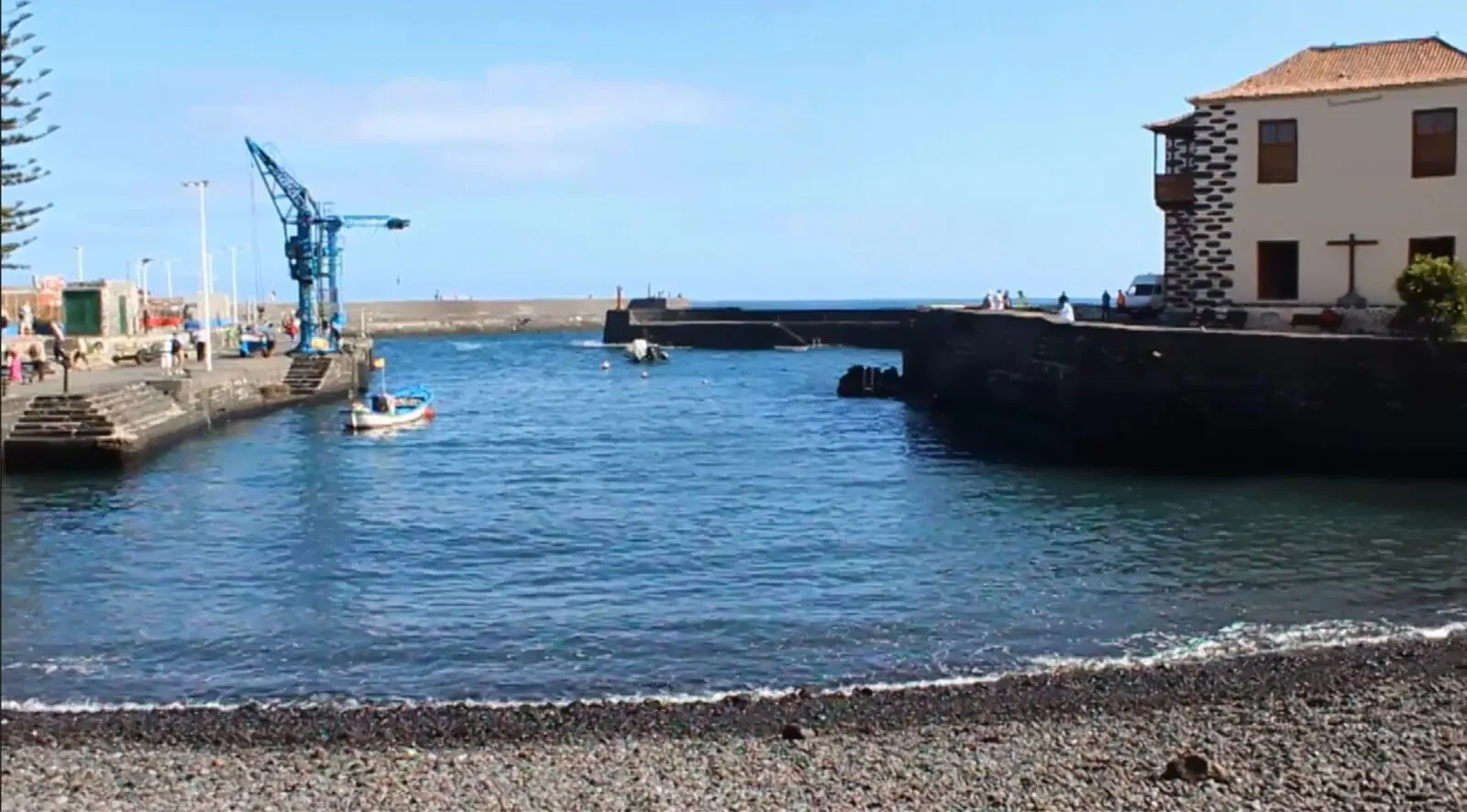 Hotel Tropical: A coastal scene with a small boat near a dock, a pier with people