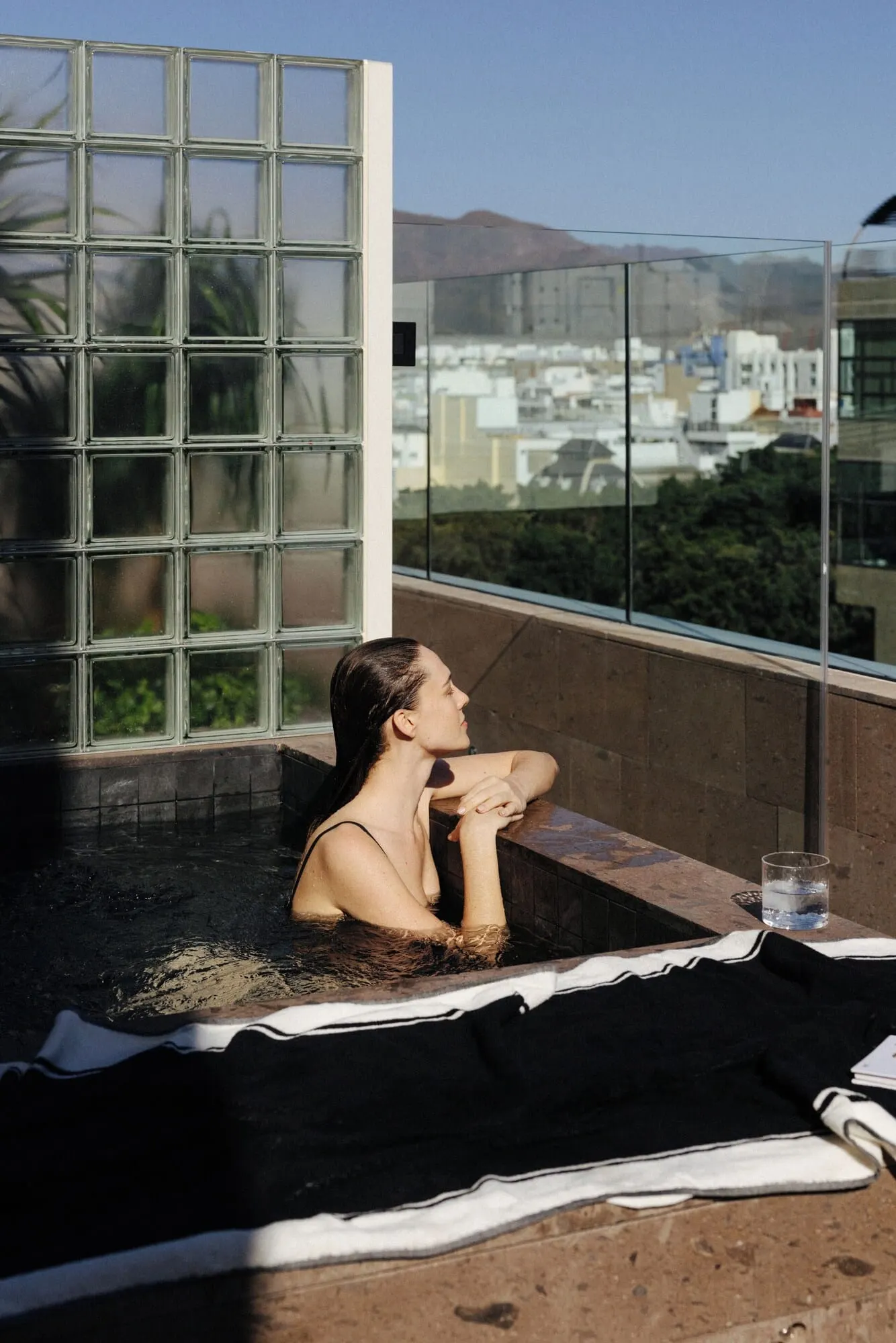 Hotel Taro Santa Cruz: A person relaxing in a hot tub with a view of buildings and mountains through a large
