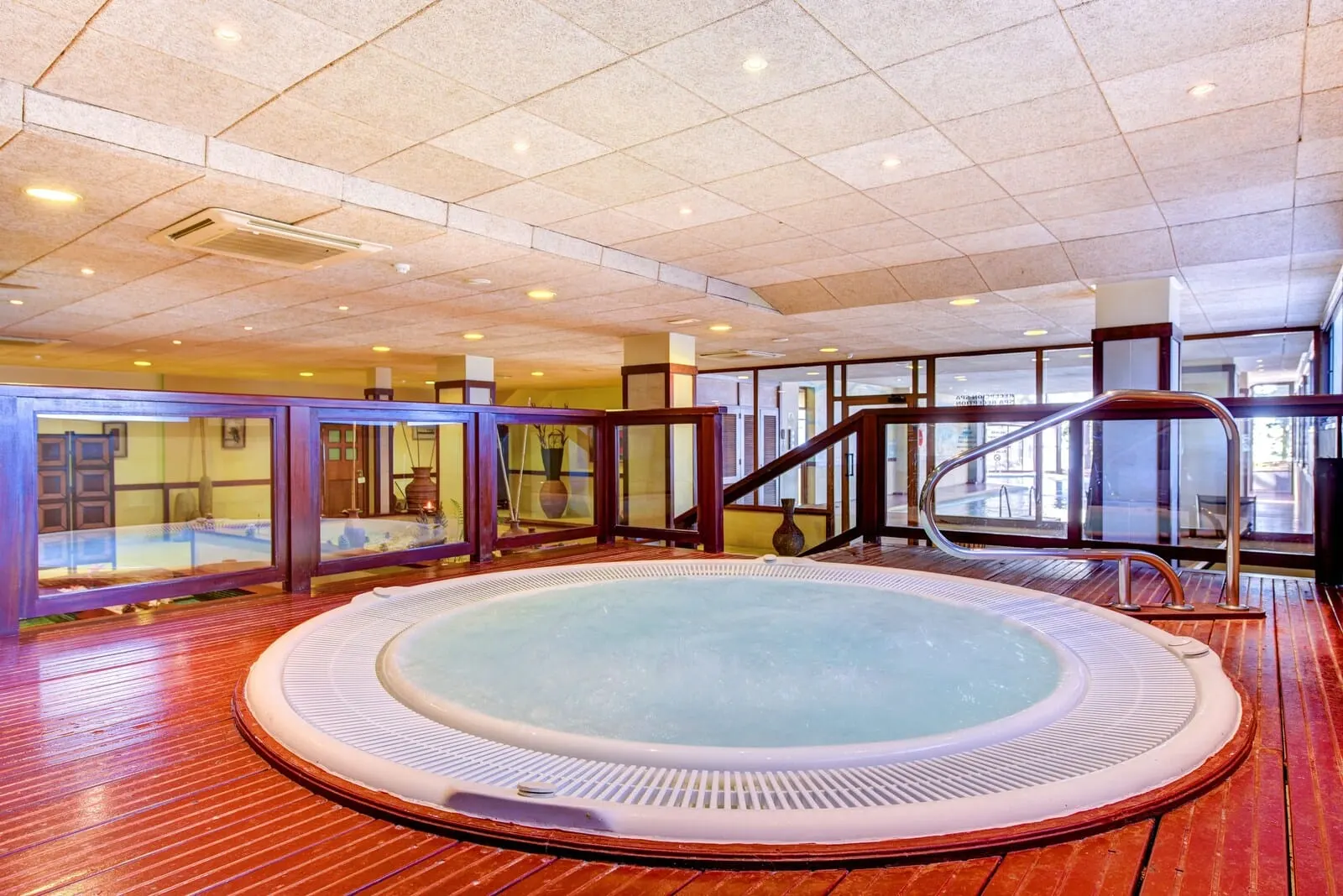 Hotel Spa Villalba: A hot tub in a room with wooden flooring, glass walls, and a staircase
