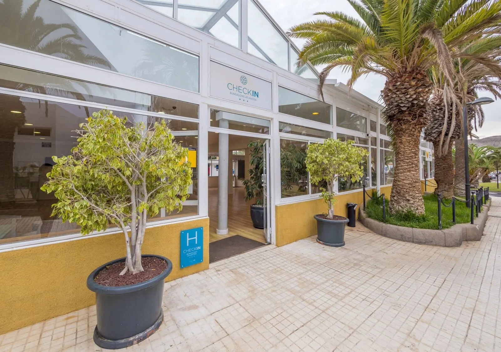 Checkin Bungalows Atlántida: A CHECKIN hotel with large windows, palm trees, and potted plants