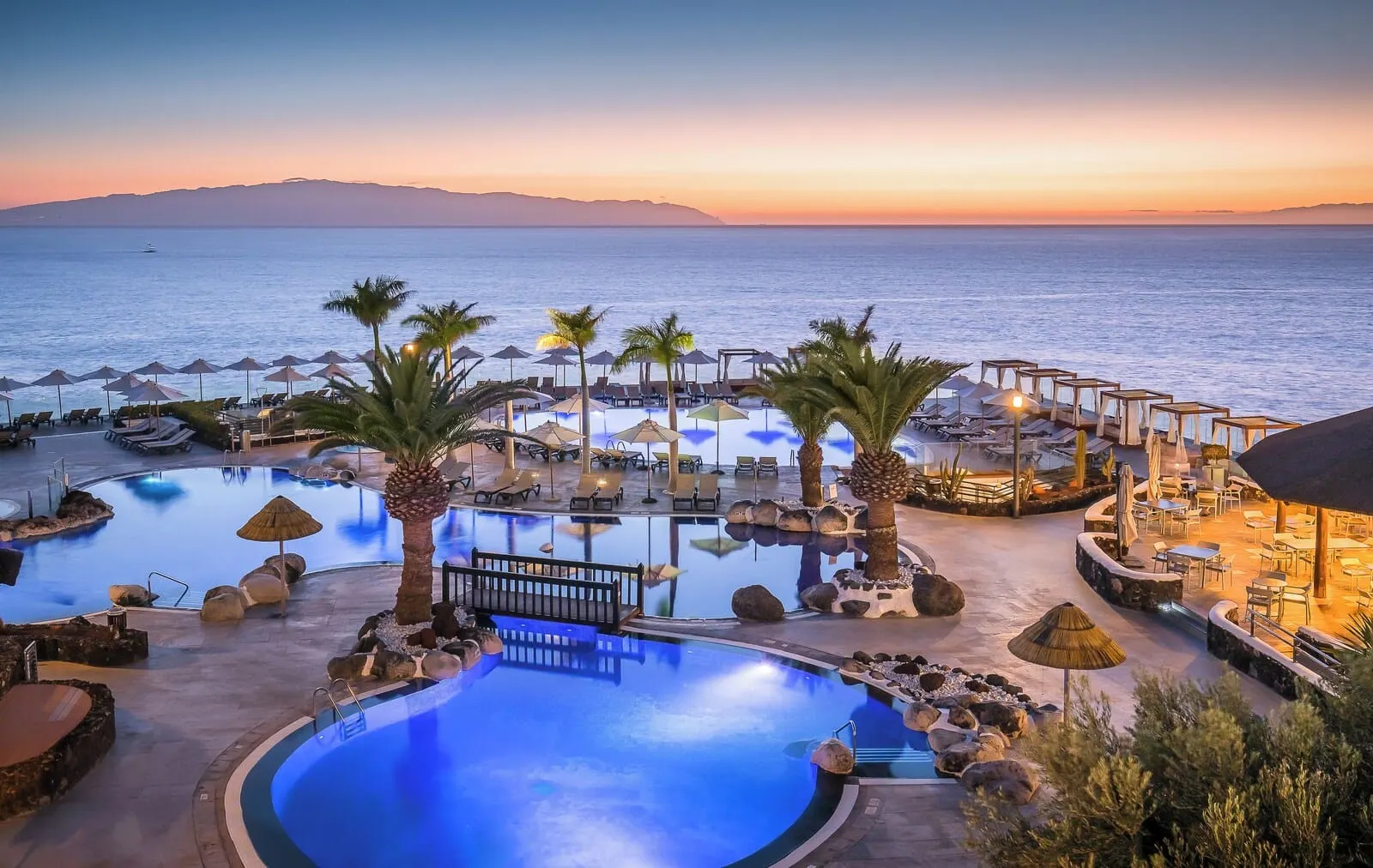 Barceló Santiago: A resort pool area with lounge chairs, umbrellas, and a view of the sea at sunset