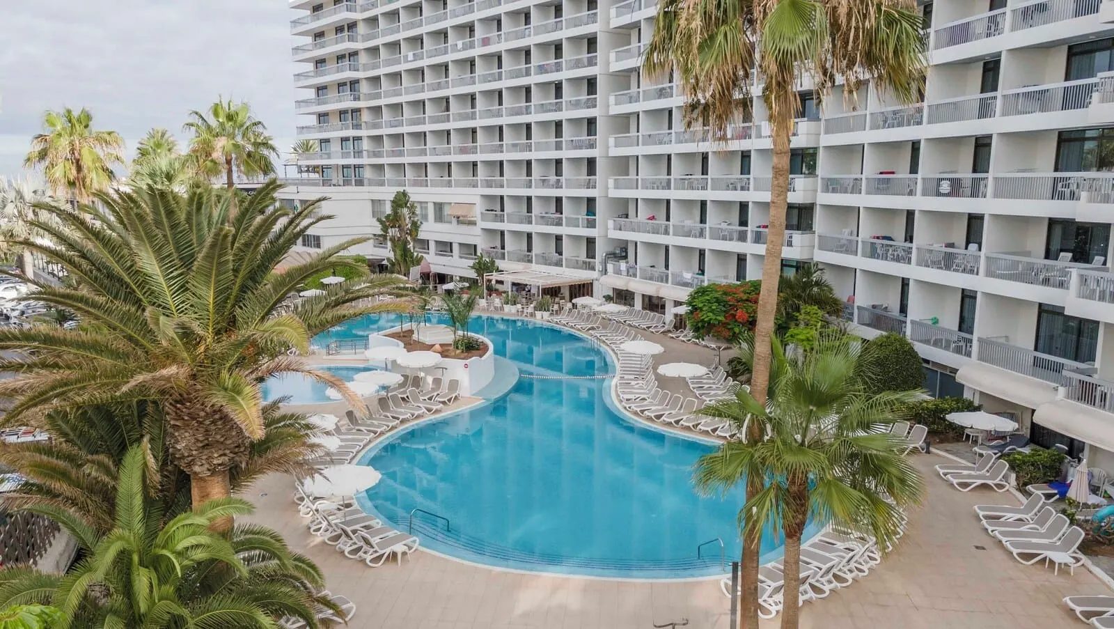 Ona Palm Beach: A hotel with a large pool surrounded by lounge chairs and palm trees