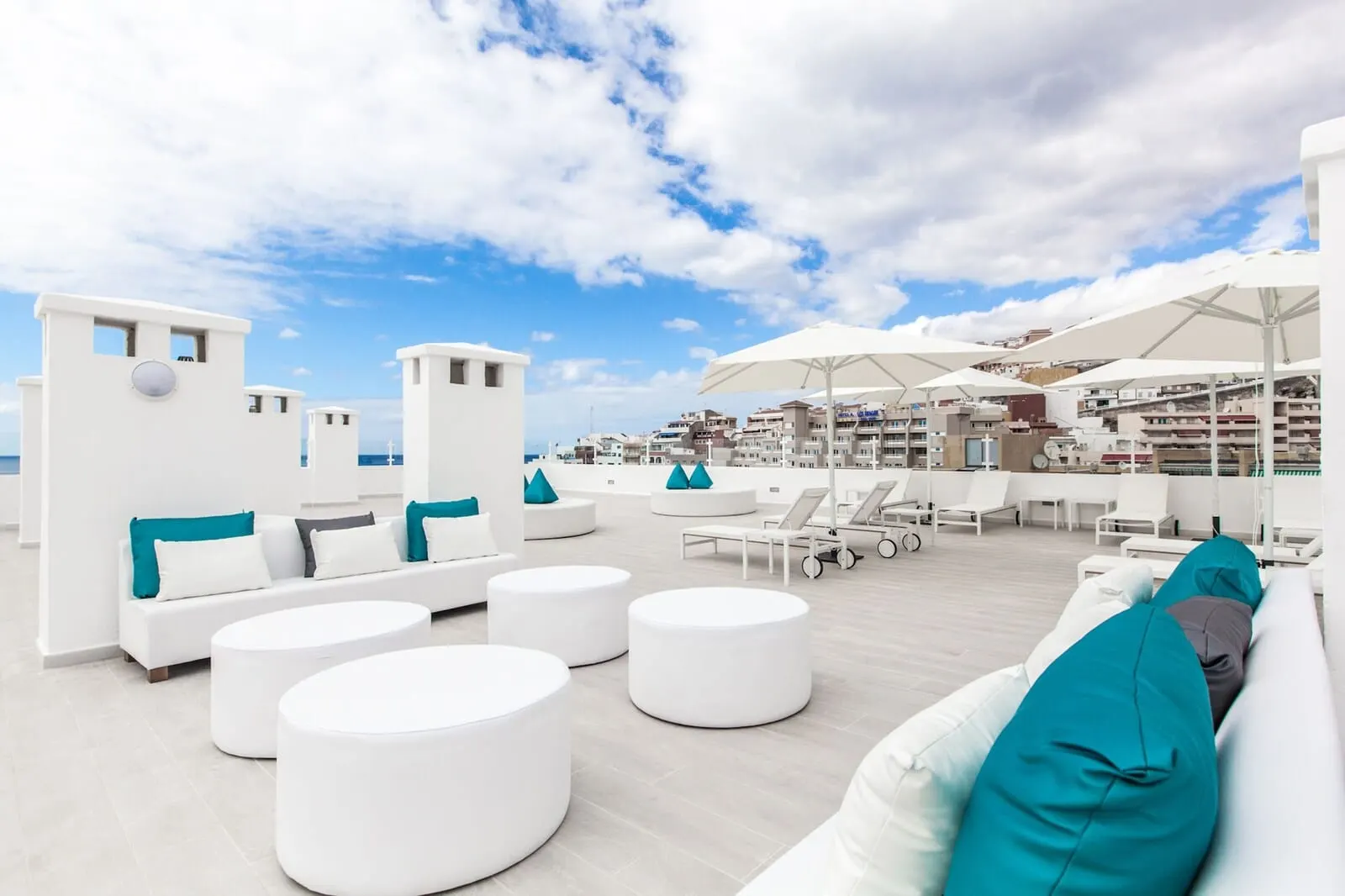BlueSea Lagos de César: A rooftop lounge with white furniture, teal cushions, and umbrellas providing shade