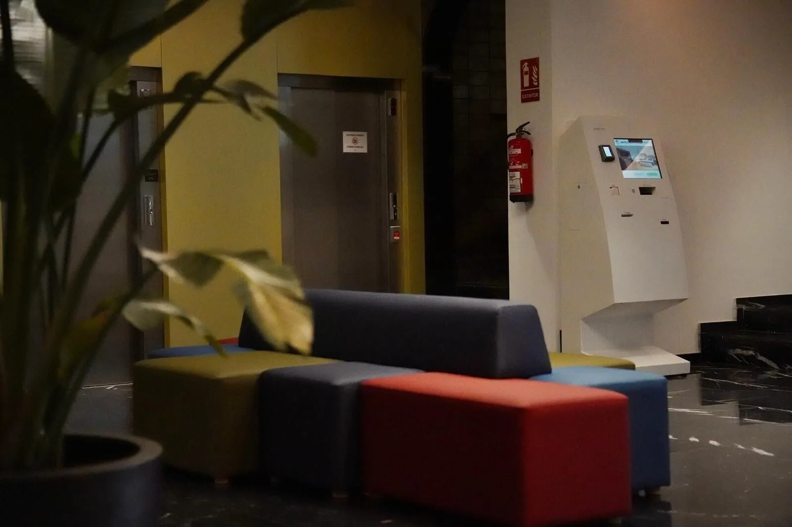 Hotel Adonis Plaza: A lobby with a sofa, a fire extinguisher, and a digital information kiosk