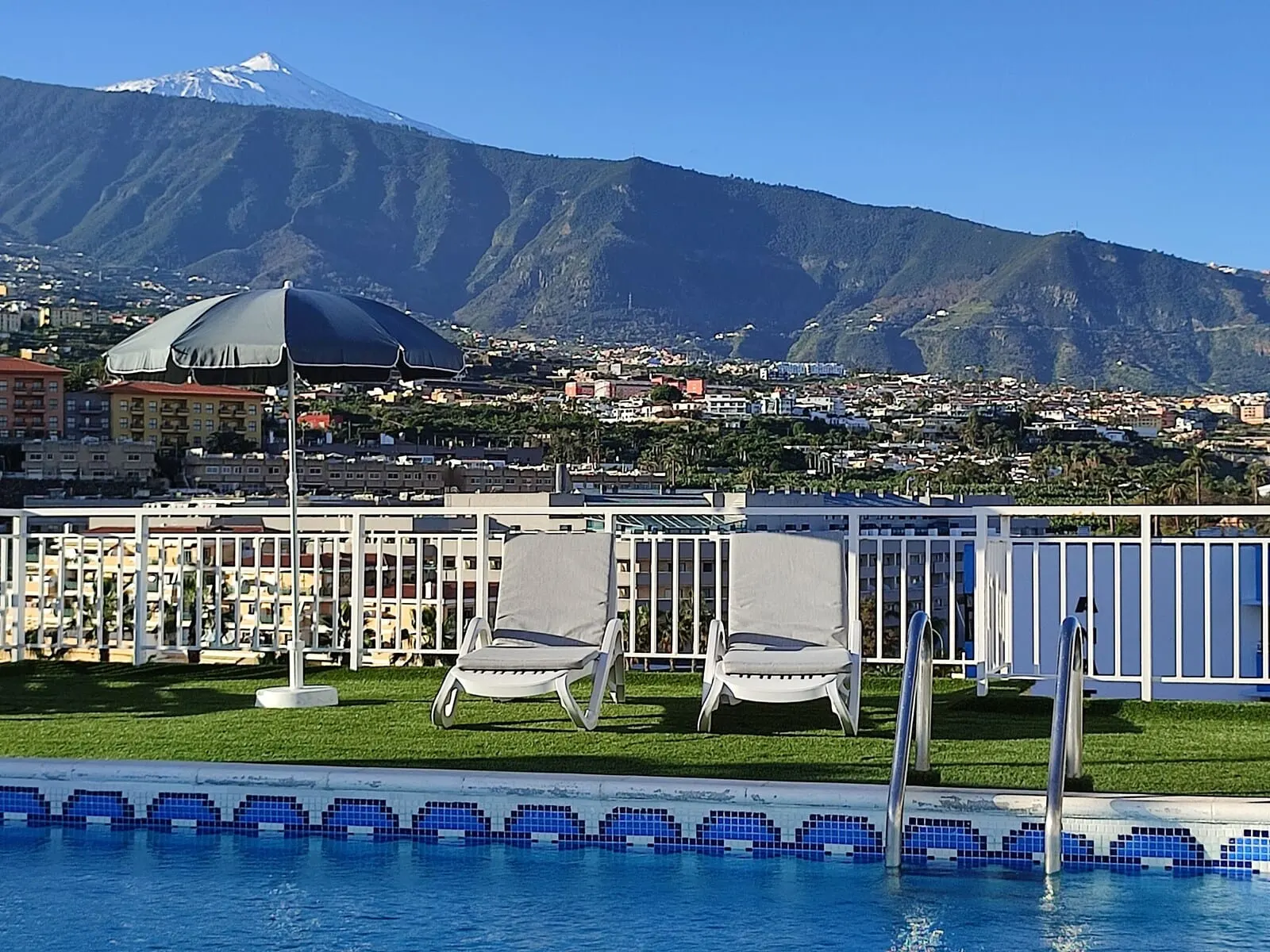 Skyview Hotel by LIVVO: A pool area with lounge chairs and a view of a mountain and town in the background