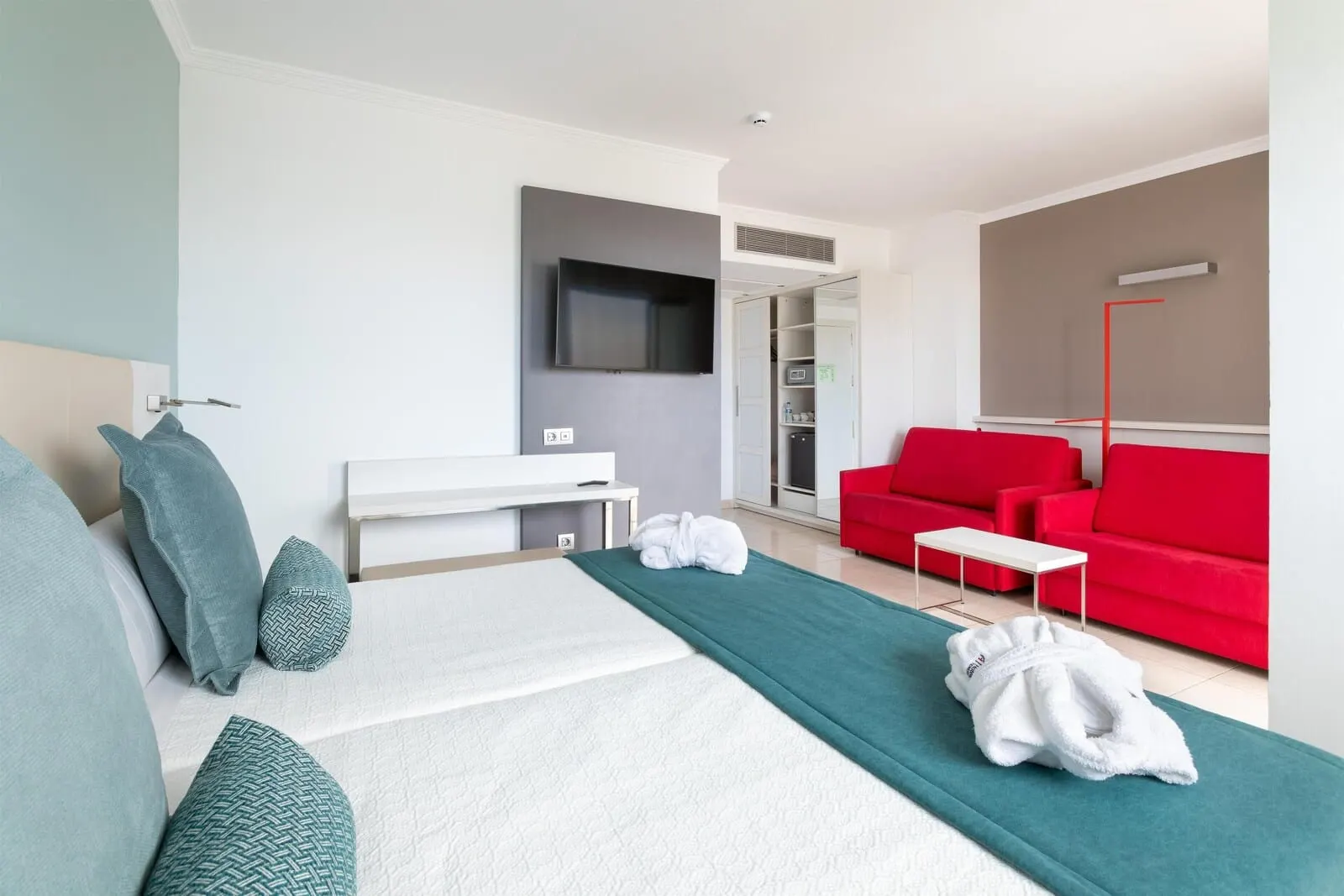Alexandre La Siesta: A modern hotel room with a bed, a red sofa, a TV mounted on the wall, and a small table