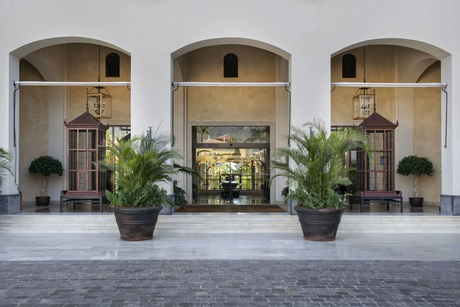 Vincci Selección La Plantación del Sur: A building entrance with three arched doorways, large potted plants, and a bench
