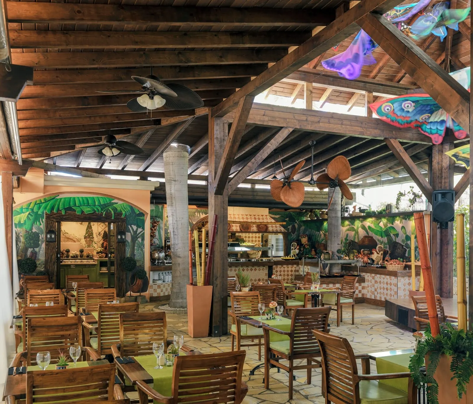 Green Garden Eco Resort & Villas: An indoor restaurant with wooden beams, green tablecloths, and a tropical mural
