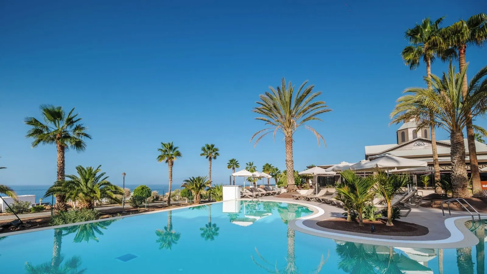 Bahia Principe Escape Tenerife: A pool with palm trees, lounge chairs, and a building with a dome