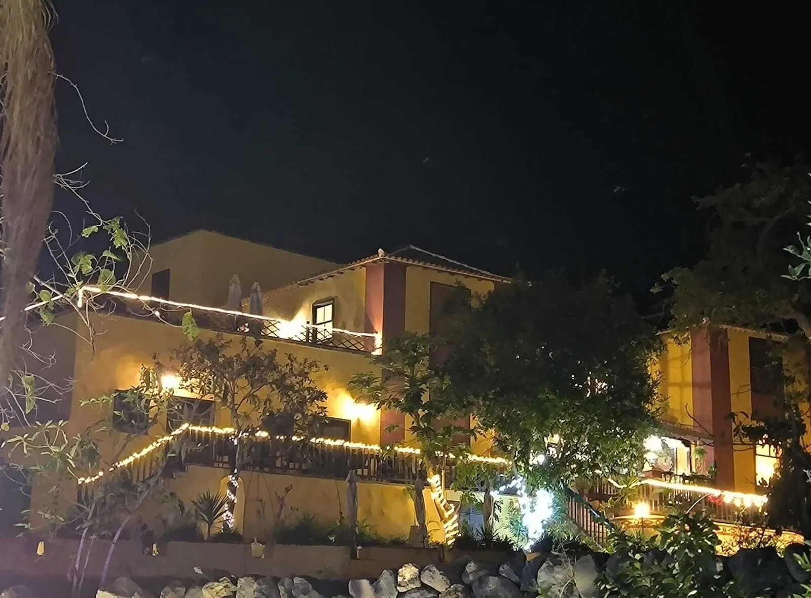 Hotel Rural La Raya 1866: A building with multiple balconies, string lights, and a well-maintained garden