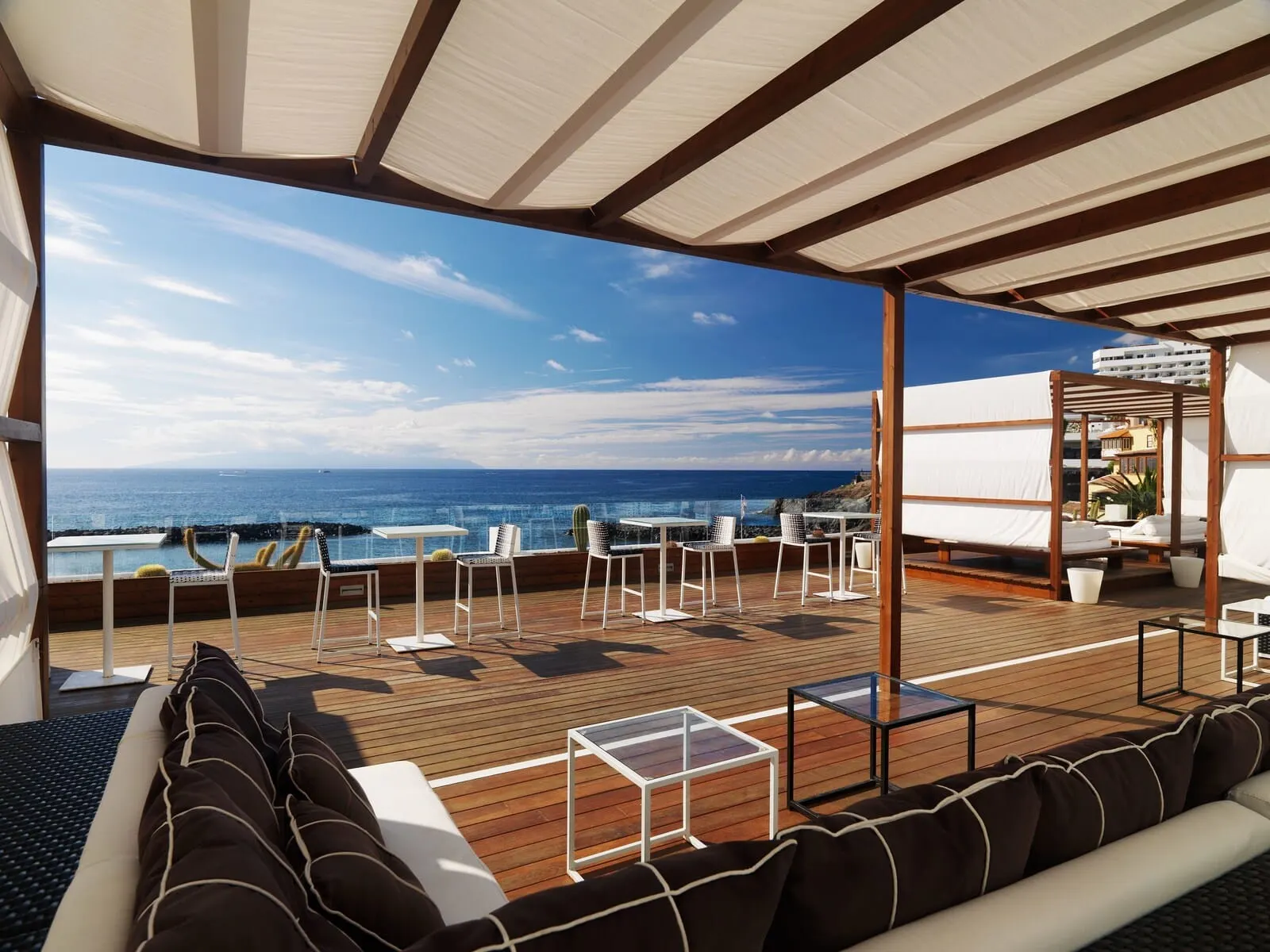 H10 Gran Tinerfe: A deck with a wooden floor, white chairs, a sofa, and a glass table