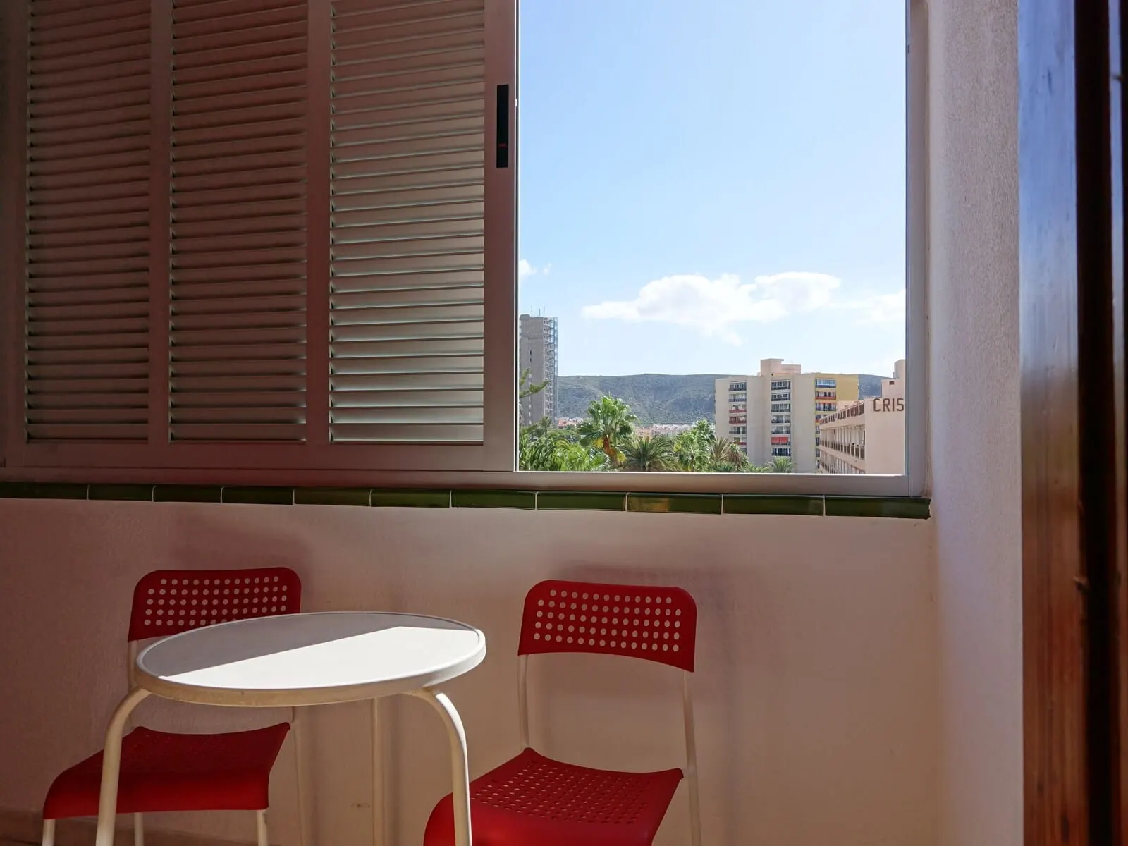 Andrea's Hotel Tenerife: A room with a window overlooking a cityscape, two red chairs, and a white table