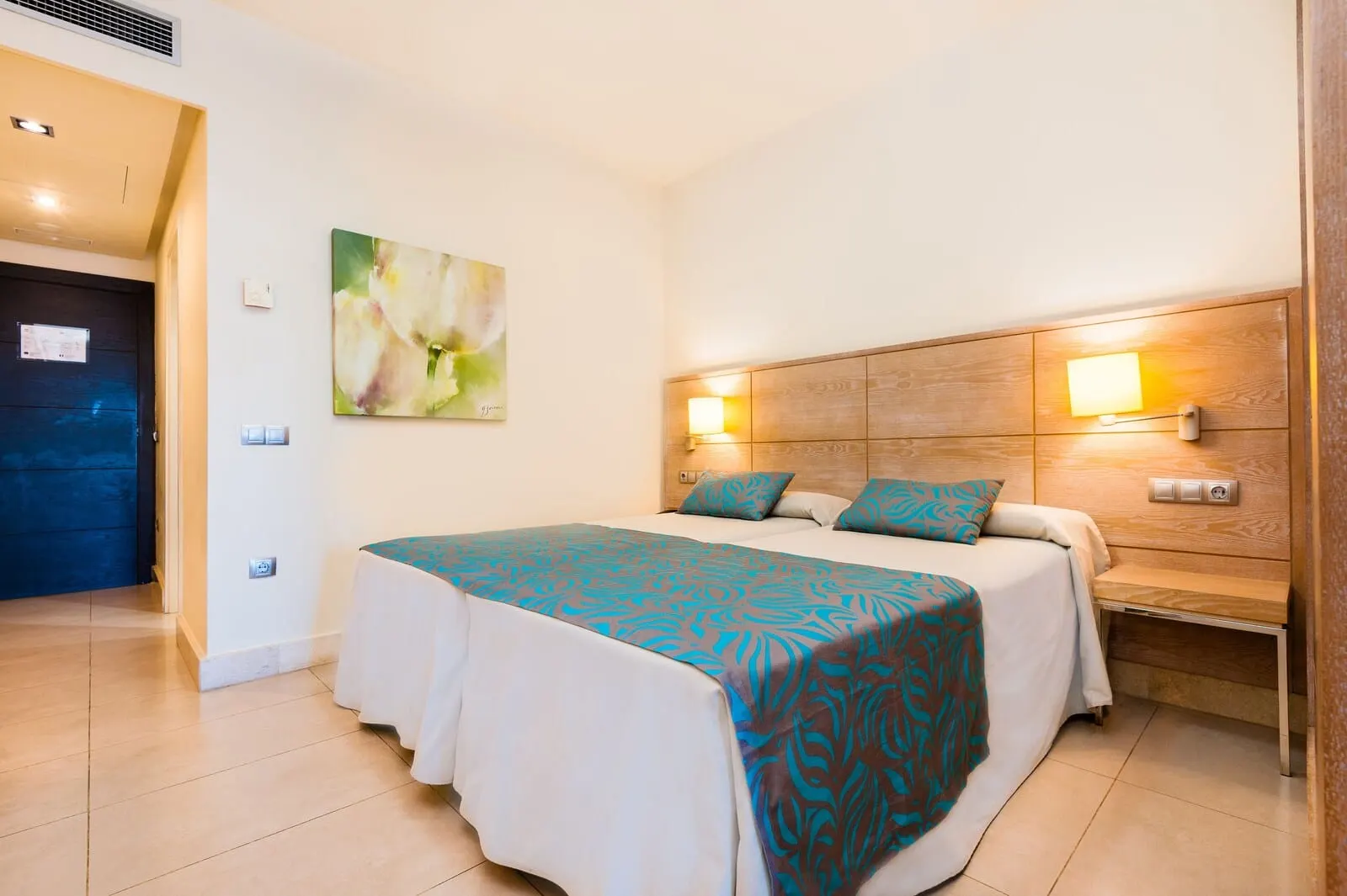 KN Hotel Arenas del Mar: A hotel room with a bed, a bench, a wall-mounted light, and a painting