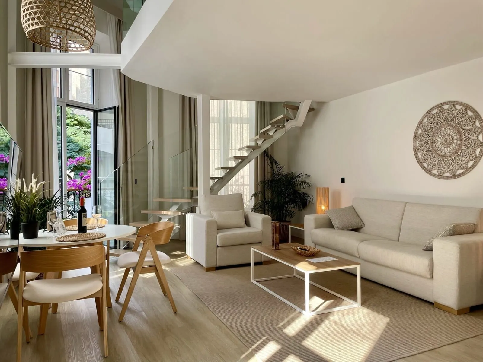 Hi Suites: A modern living room with a staircase, a dining area with a table and chairs