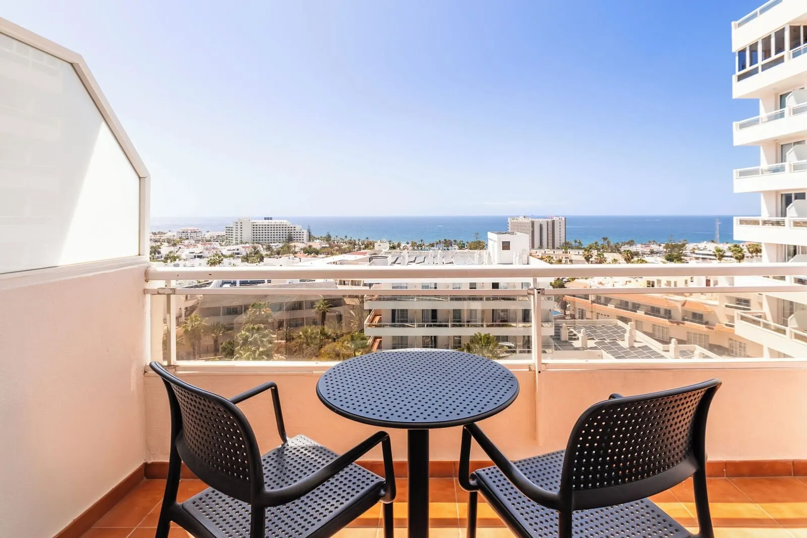 Catalonia Oro Negro: A balcony with a round table and two chairs, overlooking a coastal cityscape