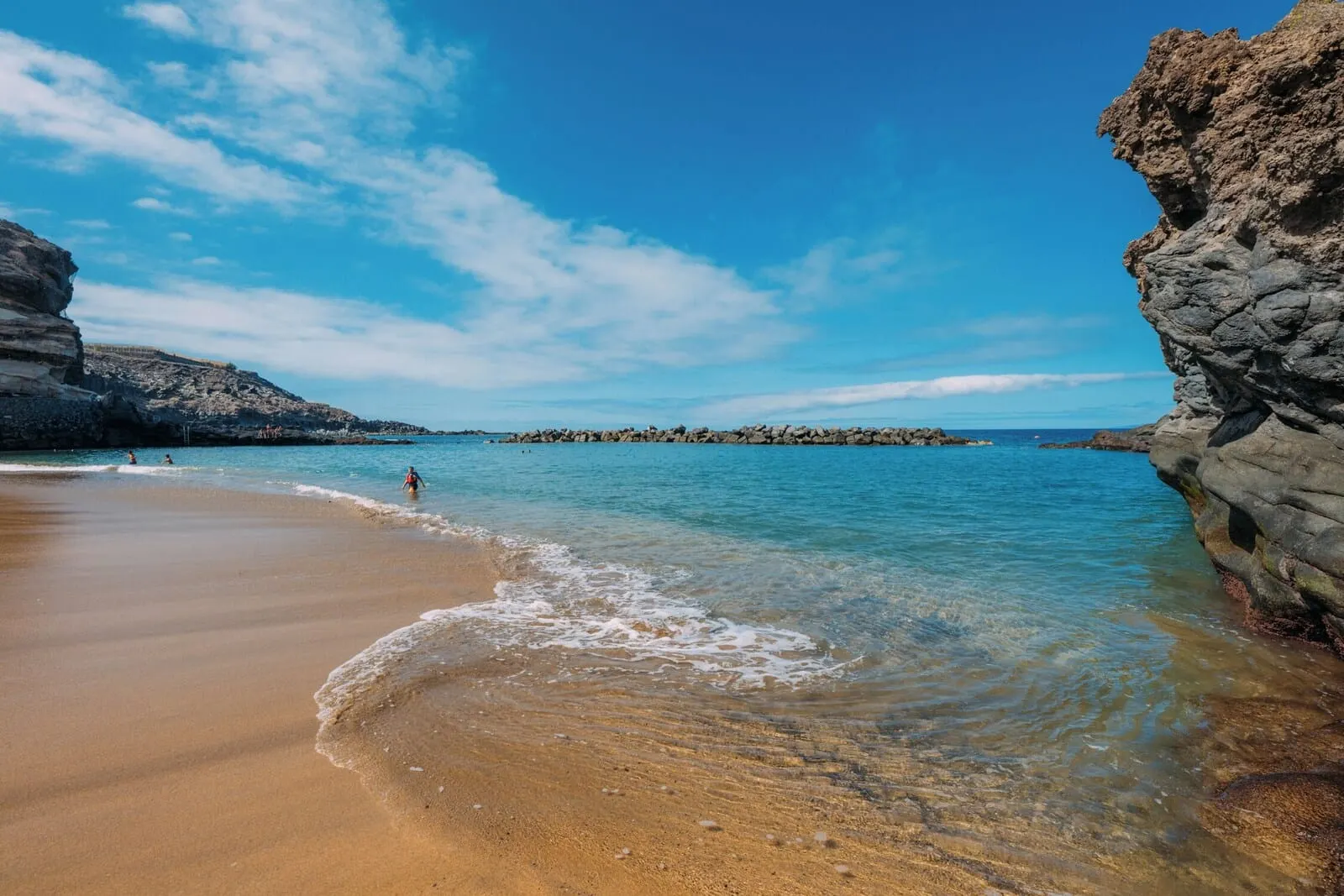 Las Terrazas de Abama Suites: A beach with clear water, rocky cliffs, and a distant rocky outcrop