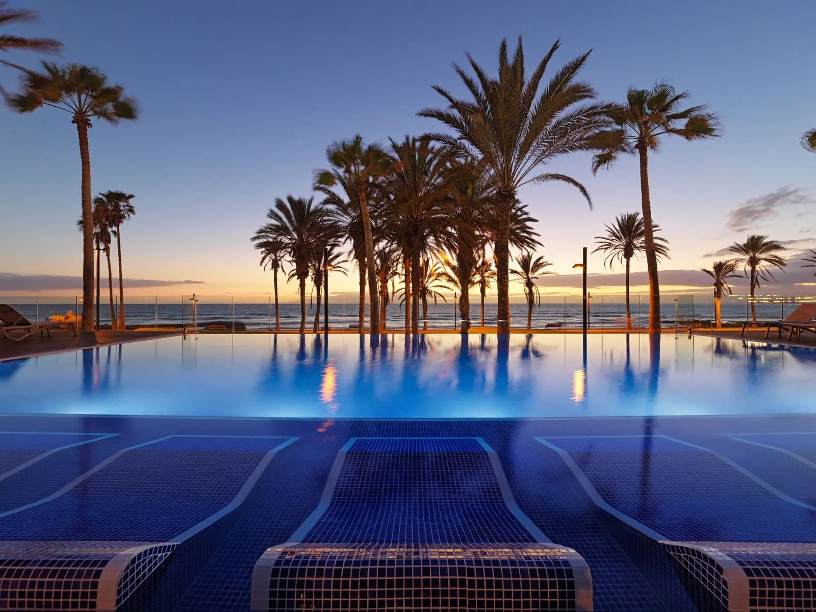 H10 Conquistador: A pool with clear blue water, surrounded by palm trees and lounge chairs