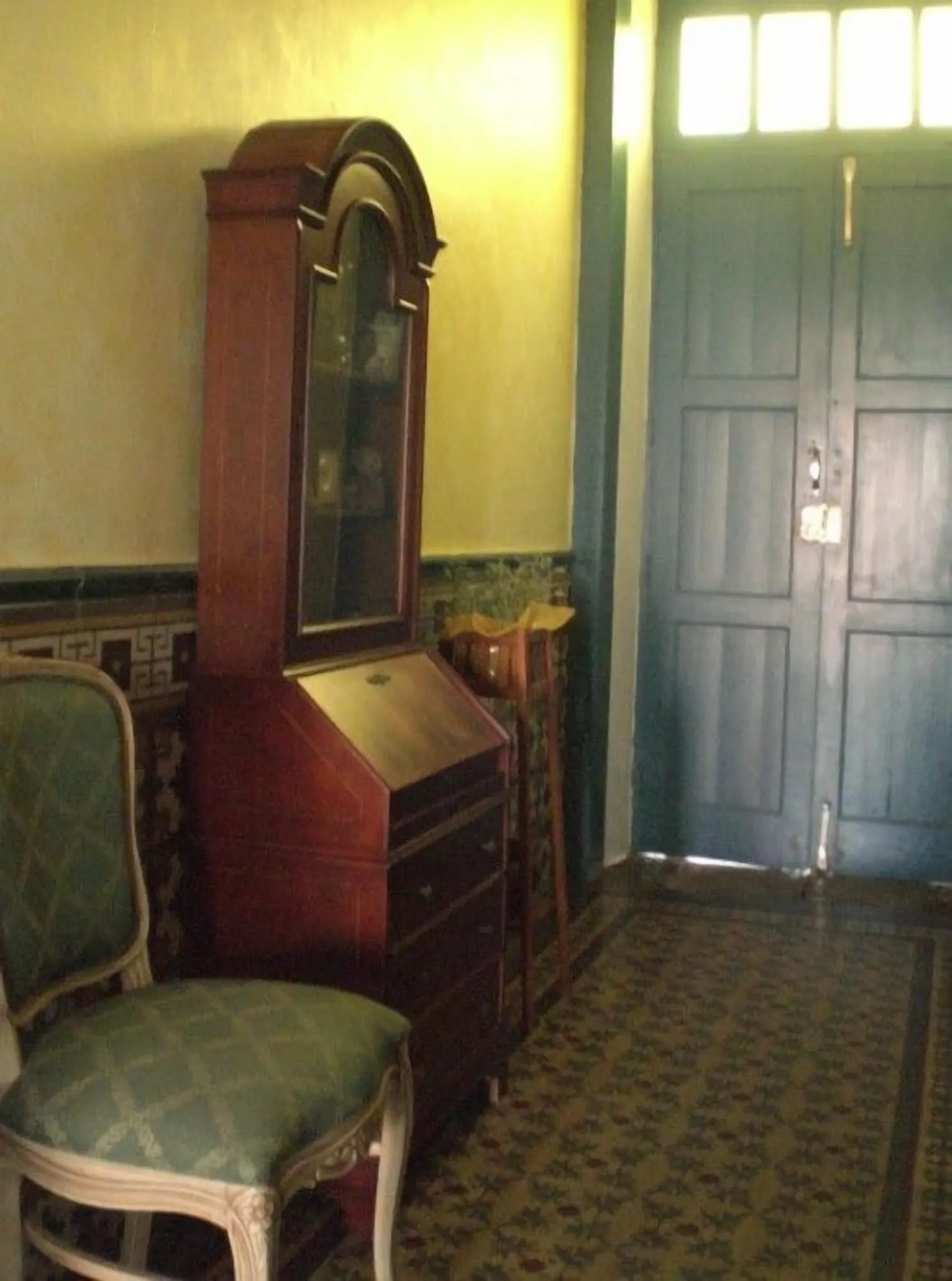 Hotel Cuatro Esquinas: A room with a green upholstered chair, a wooden dresser, and a blue door