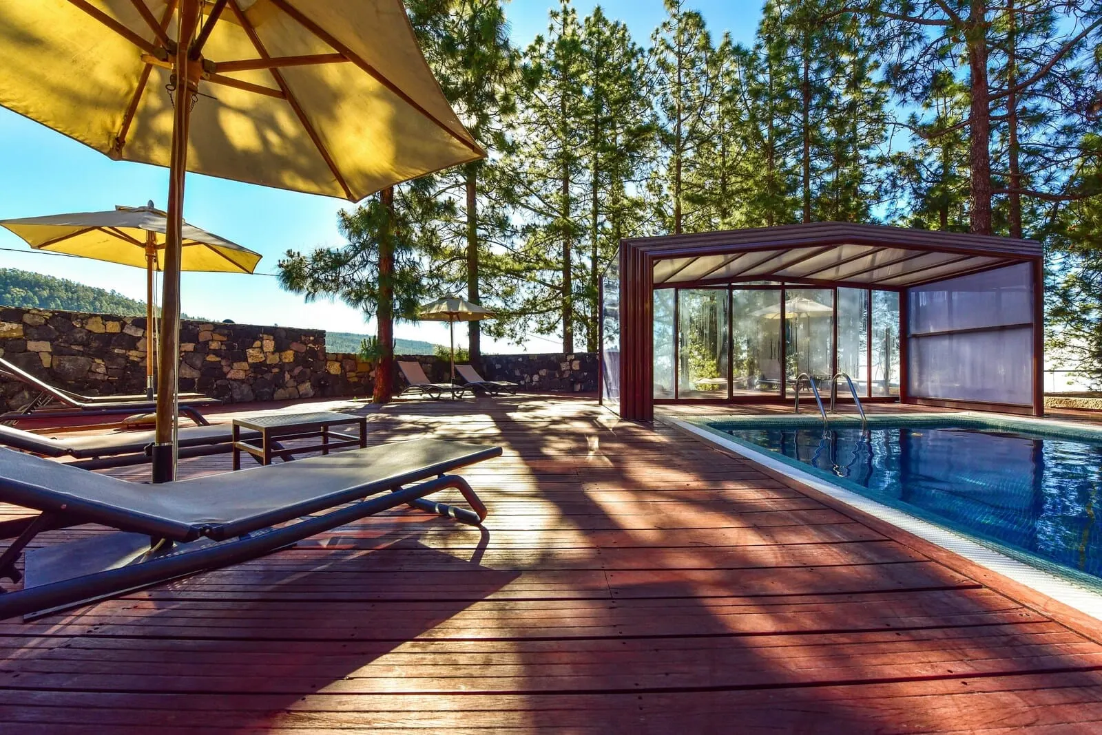 Hotel Spa Villalba: A wooden deck with sun loungers and umbrellas, a glass-enclosed pool