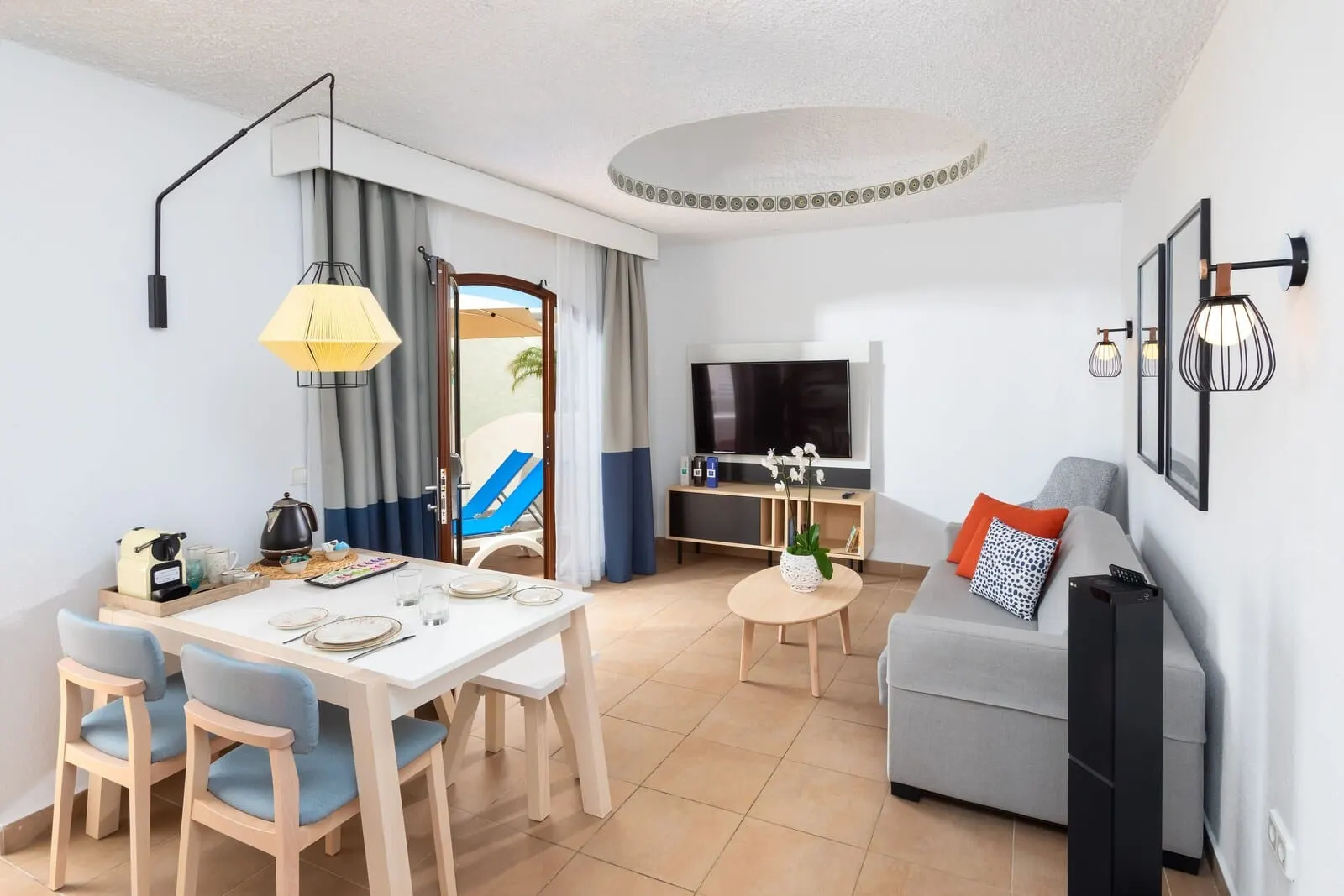 HD Parque Cristóbal Tenerife: A modern living room with a dining area, a sofa, a TV, and a small table with a plant