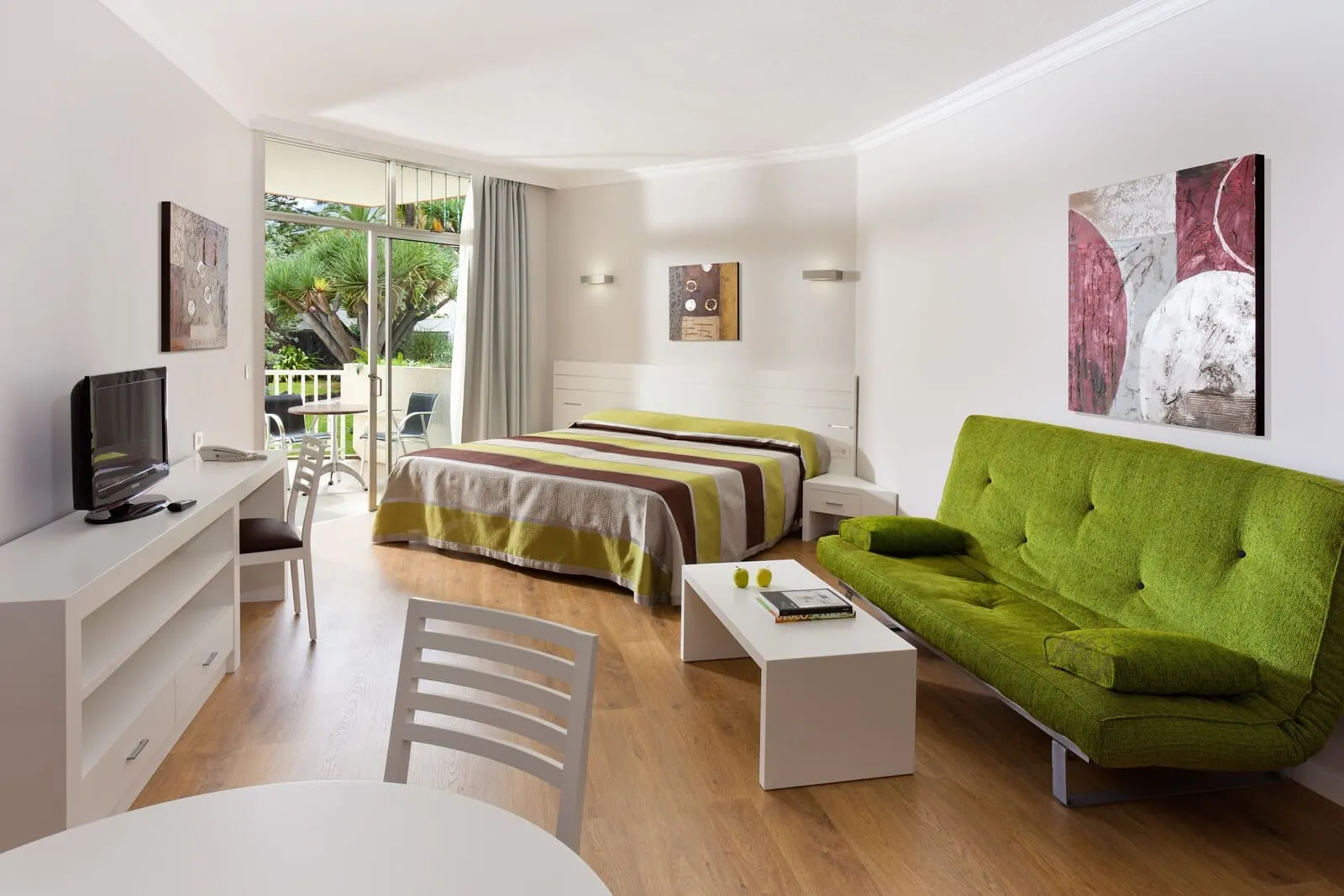Parque Vacacional Eden: A modern bedroom with a bed, a green sofa, a desk, and a TV