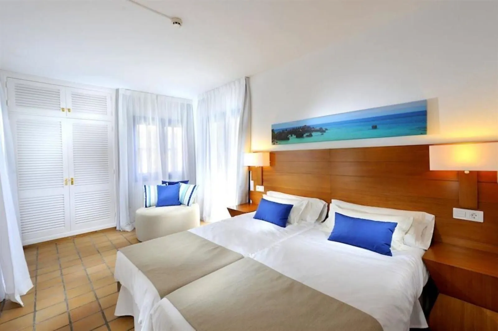 BLUESEA Bahía Fañabé Villas: A hotel room with two beds, a large window with curtains, a painting of a beach scene