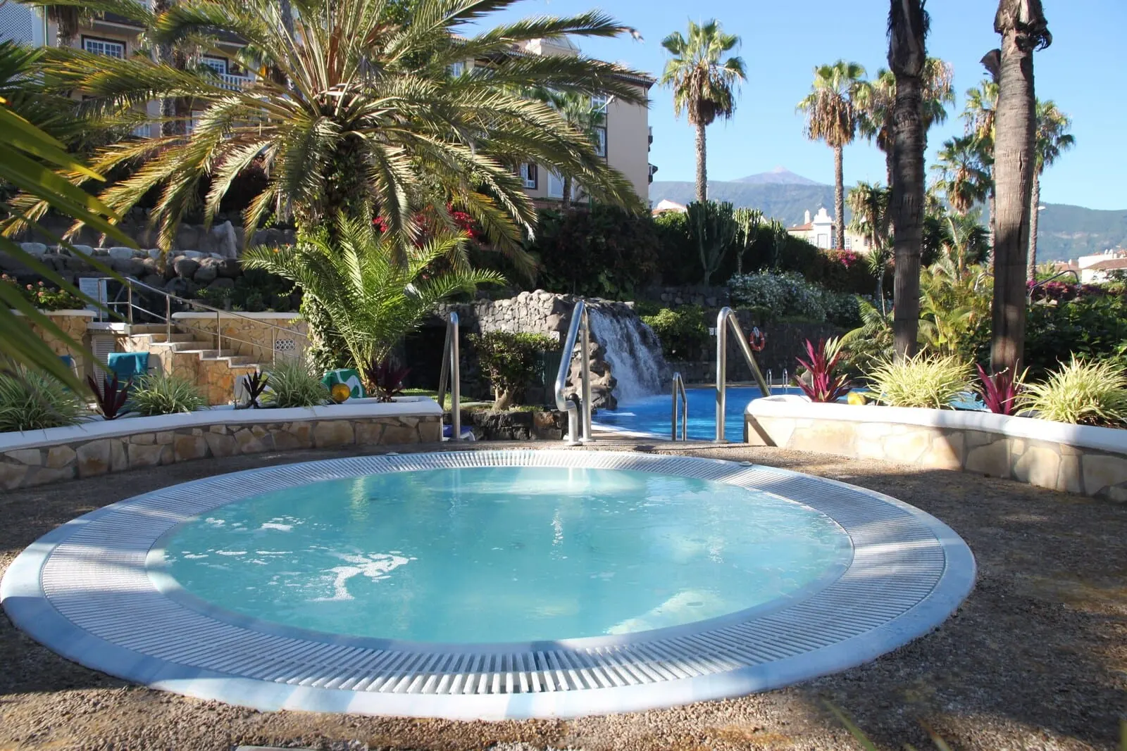 Hotel Puerto Palace: A pool with a waterfall, surrounded by palm trees and a stone wall