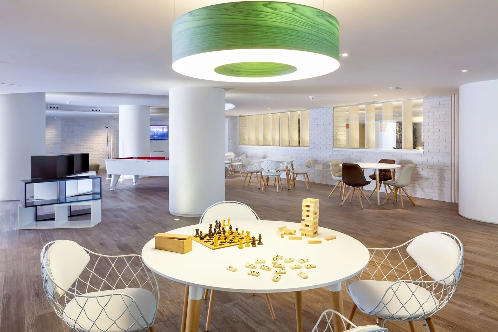 Tigotan Lovers & Friends: A modern interior with a round table set for a game, surrounded by wireframe chairs