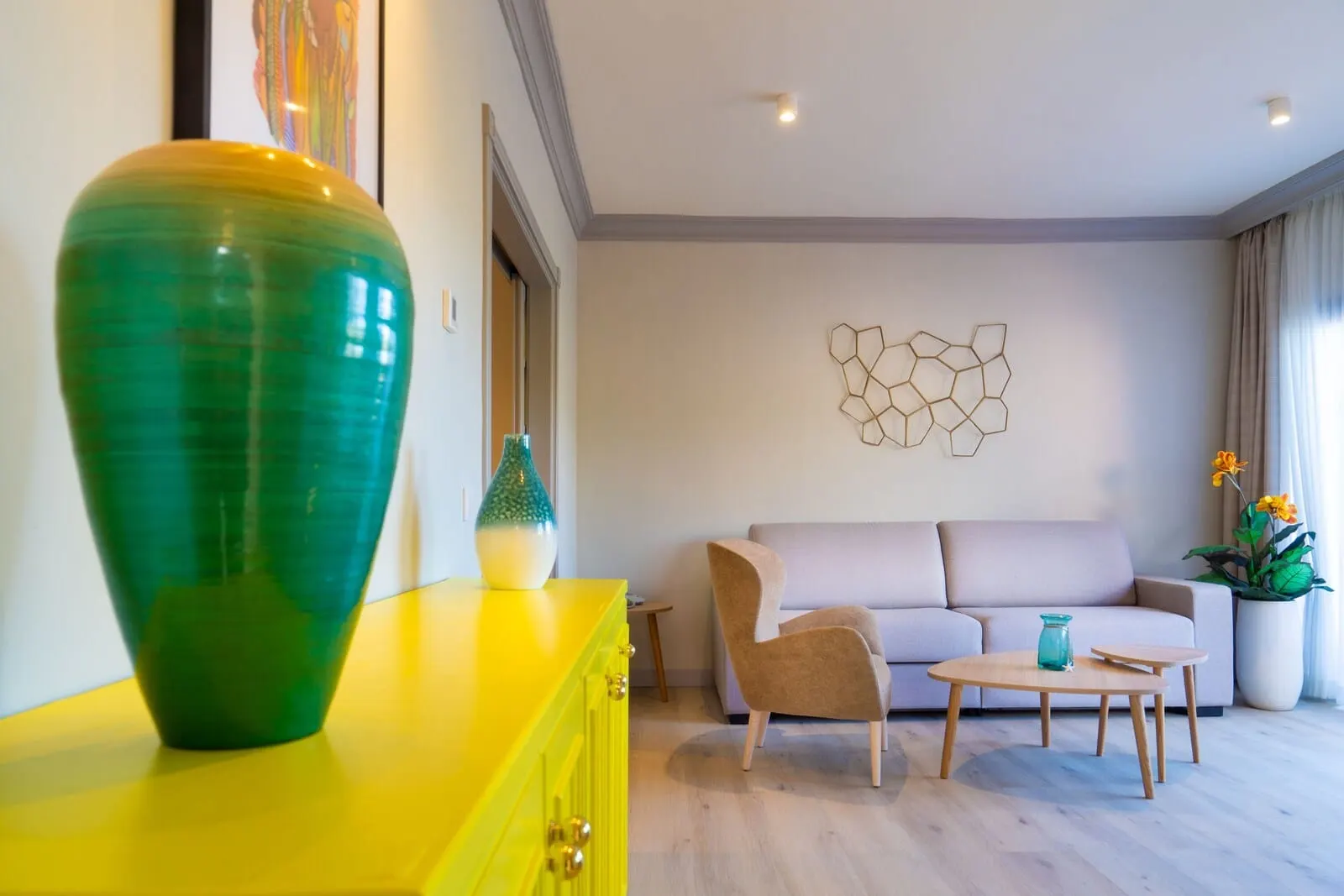 Villa Mandi Golf Resort: A modern living room with a yellow cabinet, a green vase, a beige sofa, a wooden chair