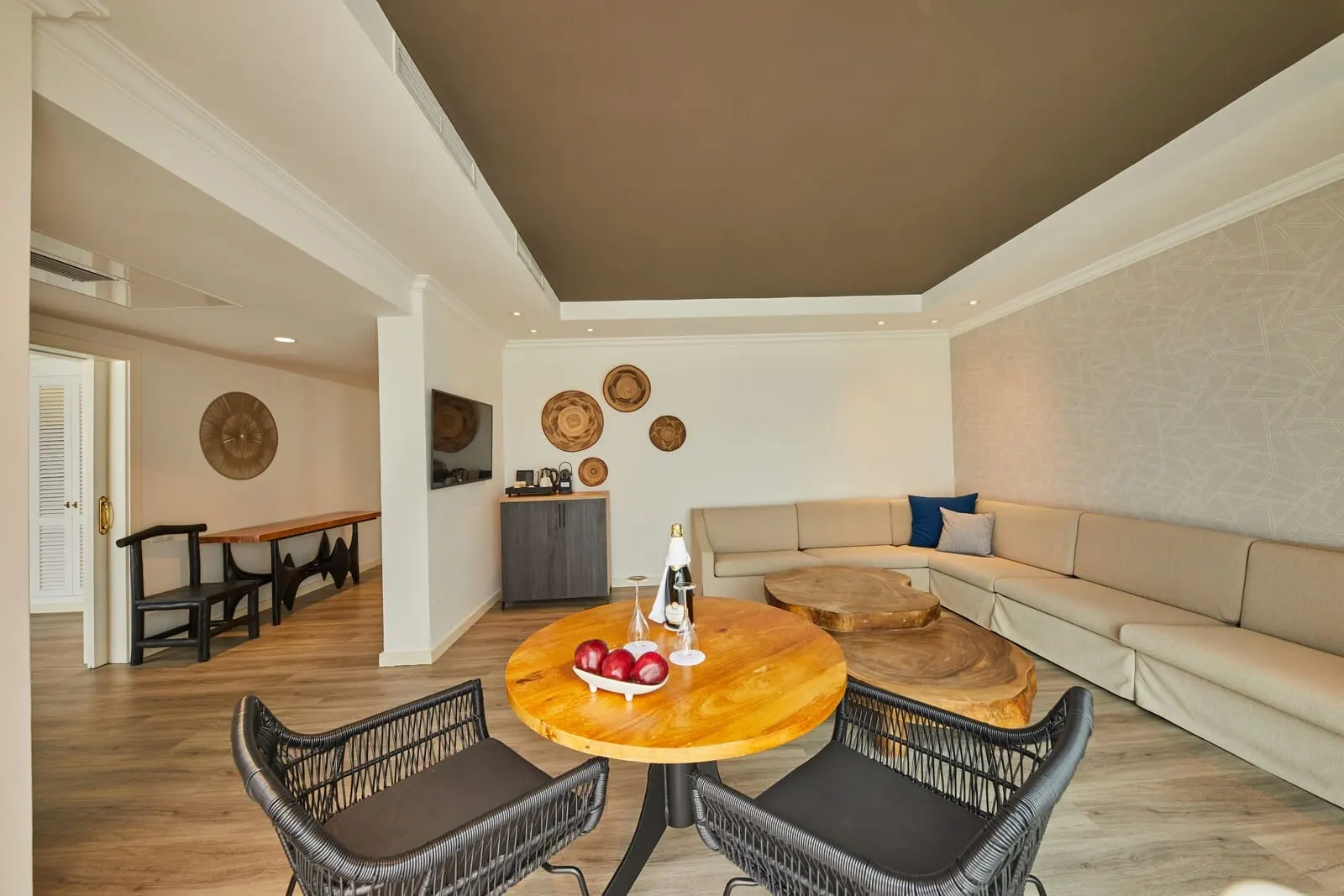 Hyatt Ziva Jardín Tropical Tenerife: A modern living room with a round wooden table, black wicker chairs, a beige sofa
