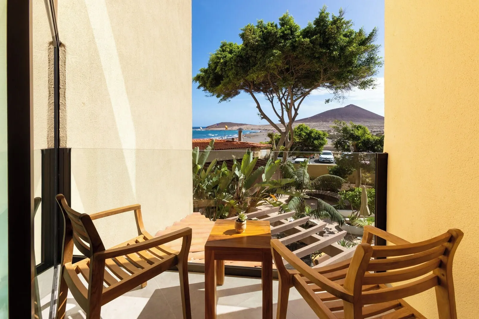 Playa Surf CBbC Hotel: A balcony with wooden chairs and a table, overlooking a beach and a mountain