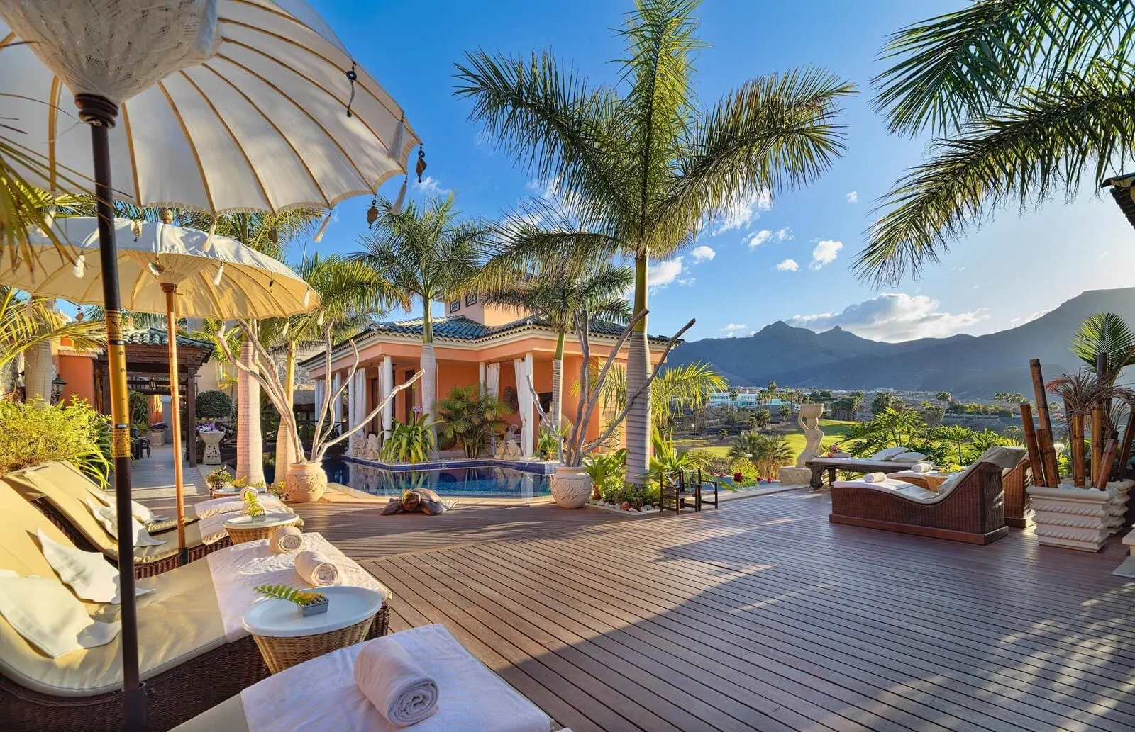 Royal Garden Villas & Spa: A wooden deck with lounge chairs and umbrellas, a pool, and a view of mountains