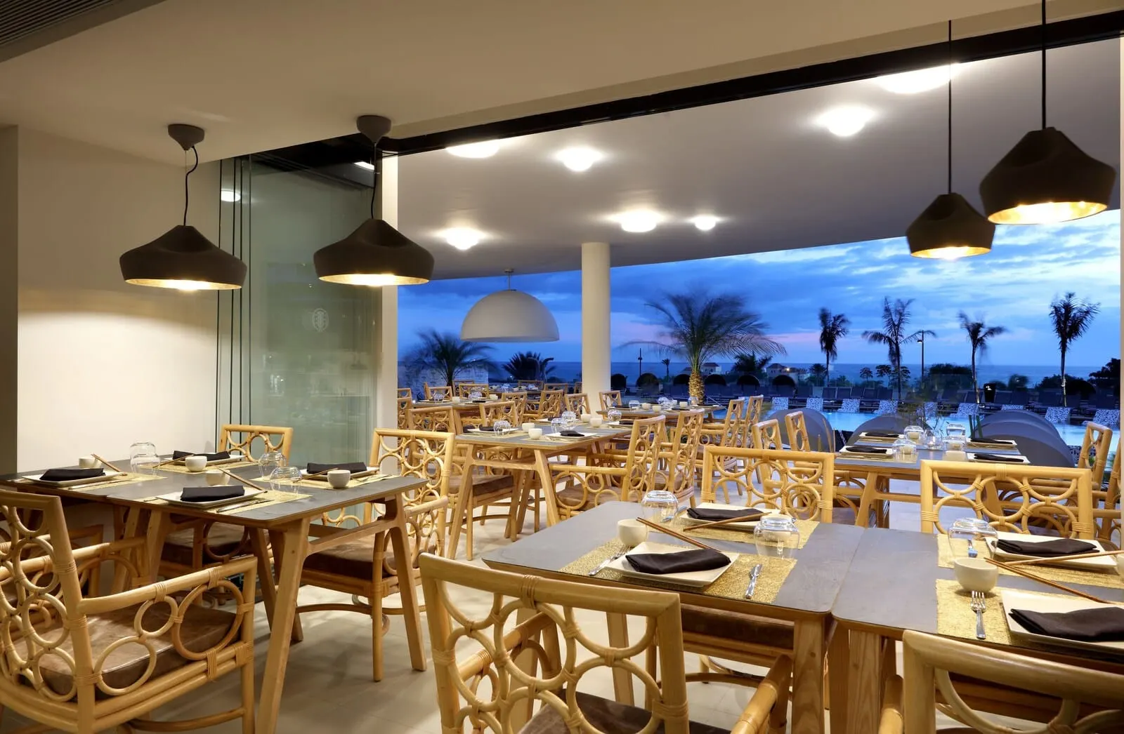 Hard Rock Hotel Tenerife: A restaurant with wooden furniture and tables set for dining, large pendant lights