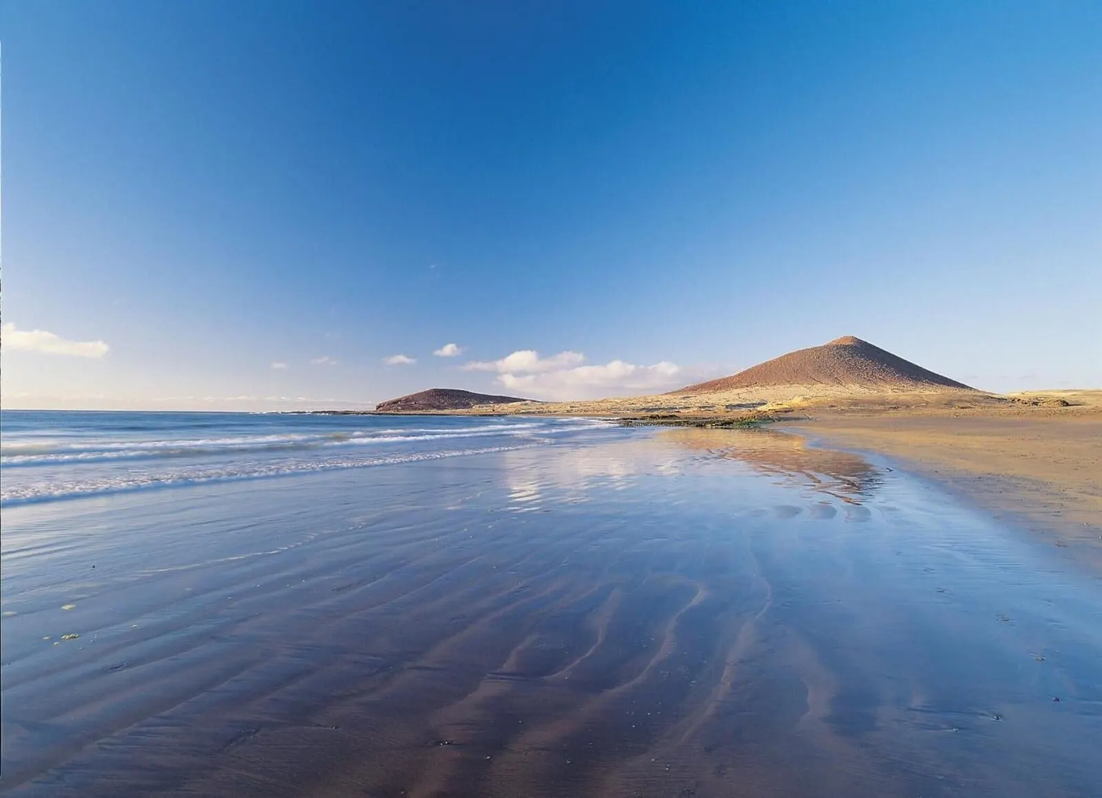Médano Hotel: A beach with a sandy shore and a hill in the background