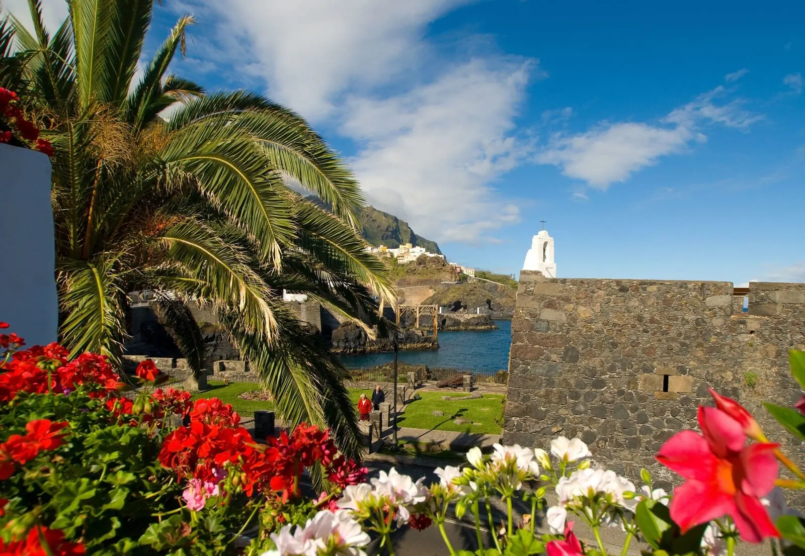 Garahotel: A coastal view with a white church, stone walls, and red flowers in the foreground