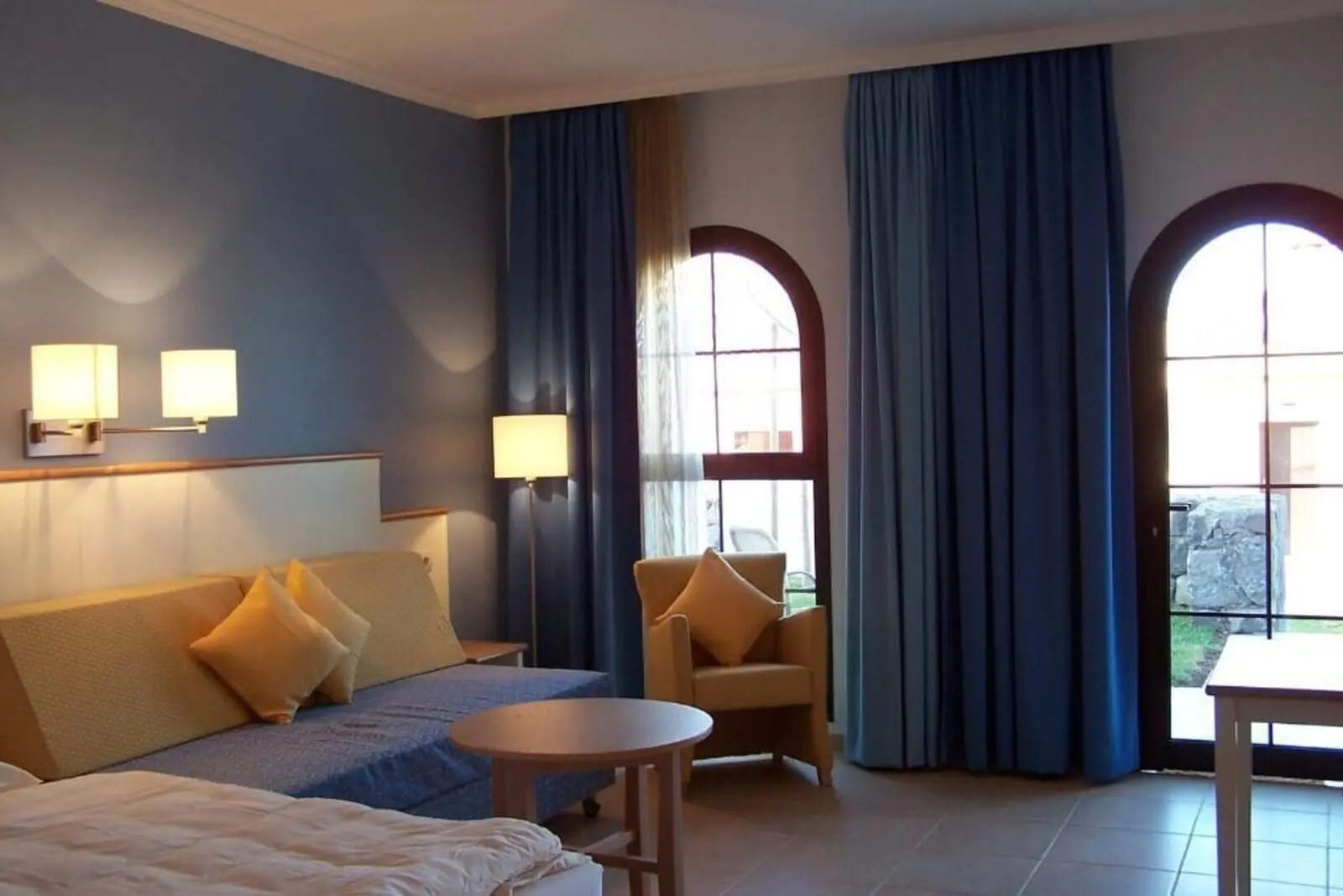 Hotel Luz del Mar: A hotel room with a bed, a sofa, a chair, a small table, and two windows with curtains